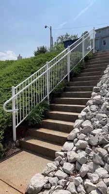 Outdoor concrete stairs with white handrails beside a stone retaining wall and grassy slope