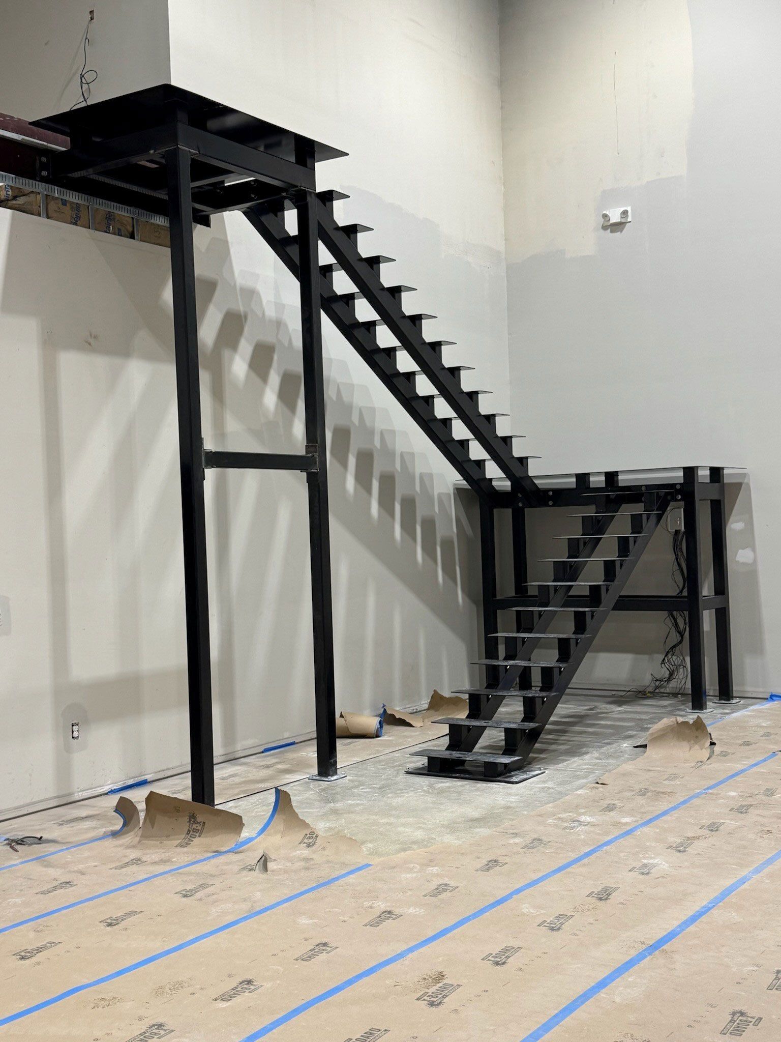 Black metal staircase structure in an unfinished room with concrete floor and white walls