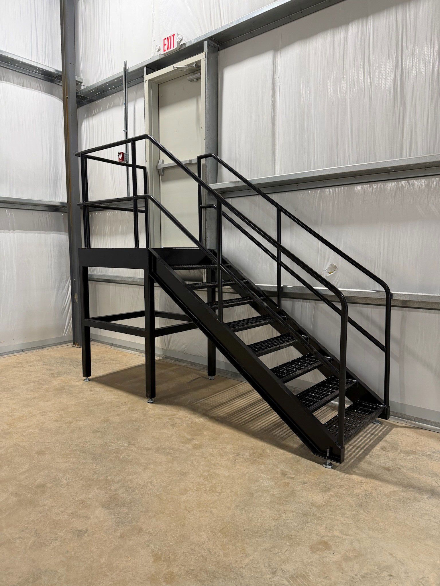 Black metal staircase with railings in an industrial warehouse interior.