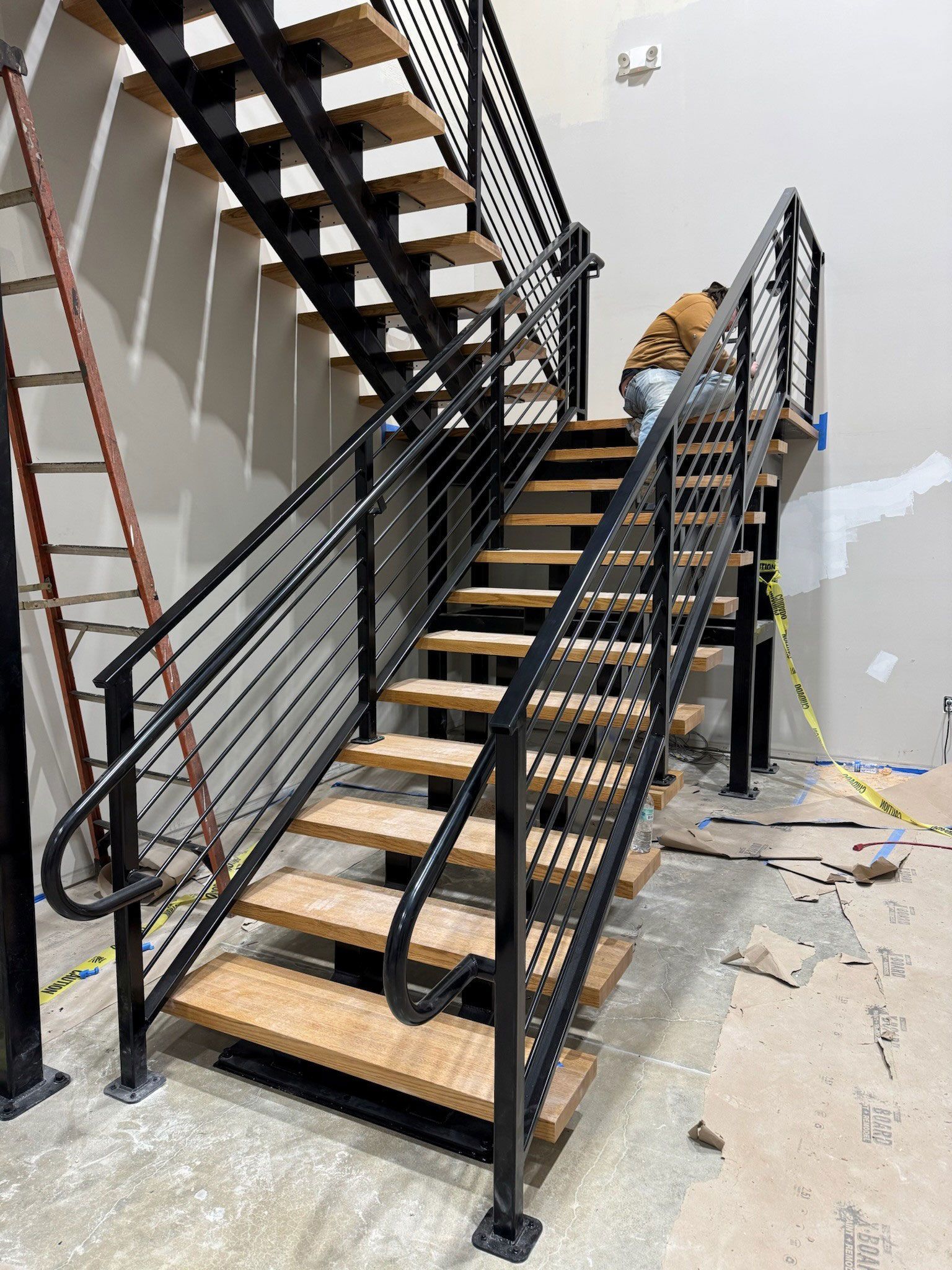 Interior staircase under construction with black railings and wooden steps, debris on the floor