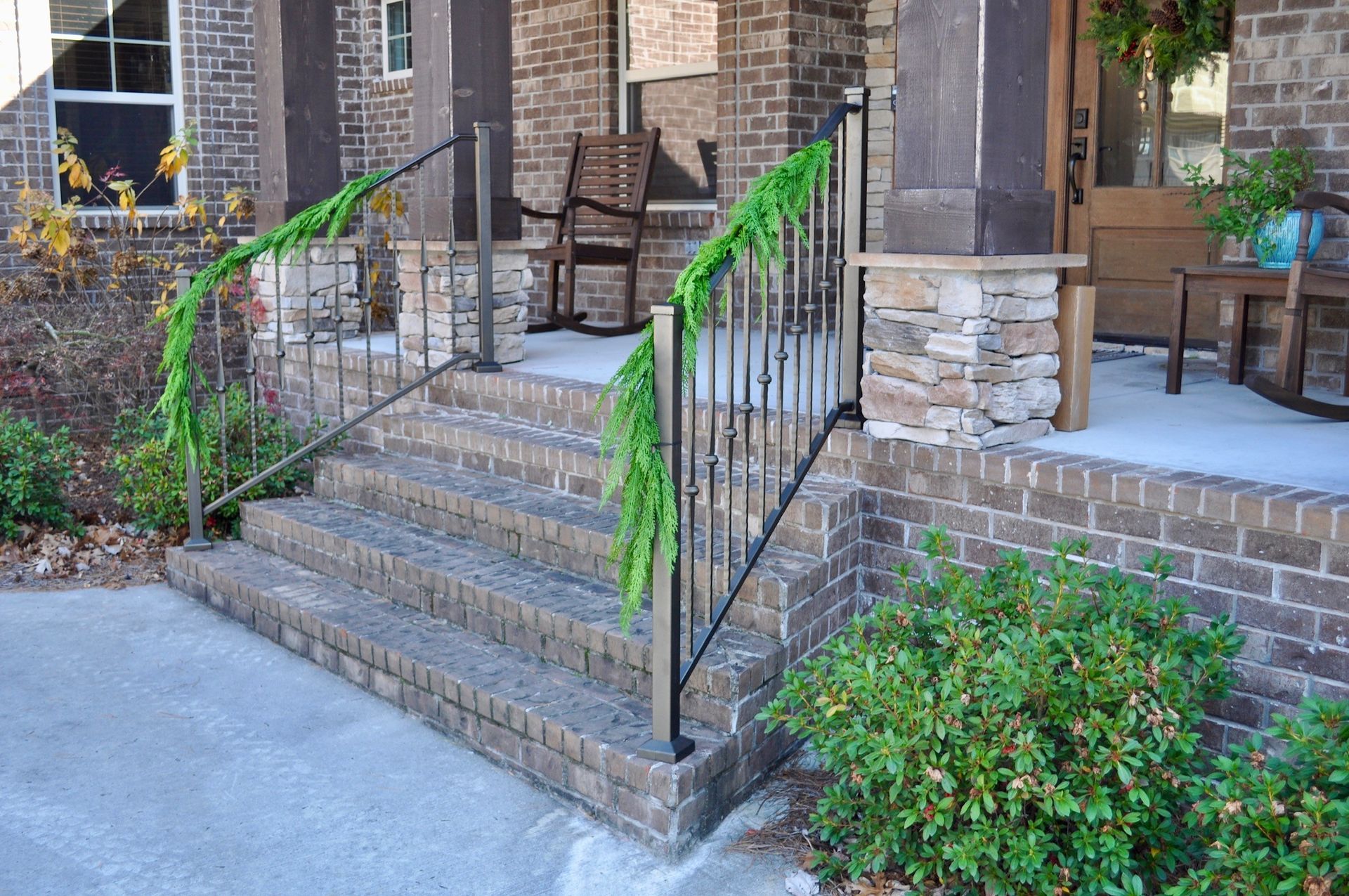 Brick front steps with black railings leading to a house entrance, flanked by greenery.