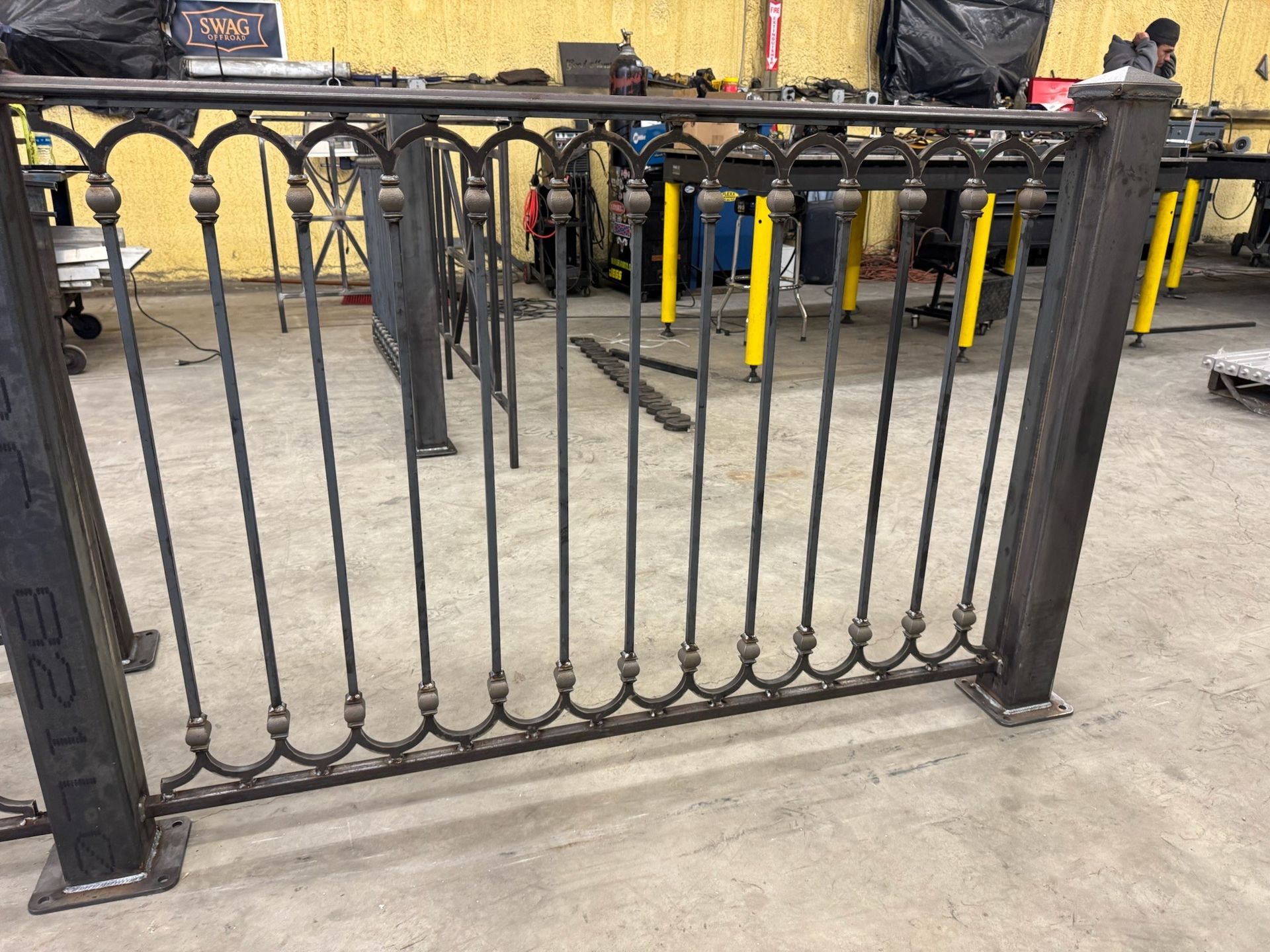 Black wrought-iron gate with decorative scrollwork in a workshop or garage.
