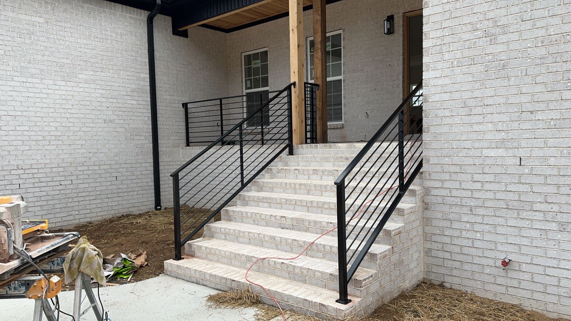 Front porch with concrete steps, black railings, and white brick walls on a house exterior.