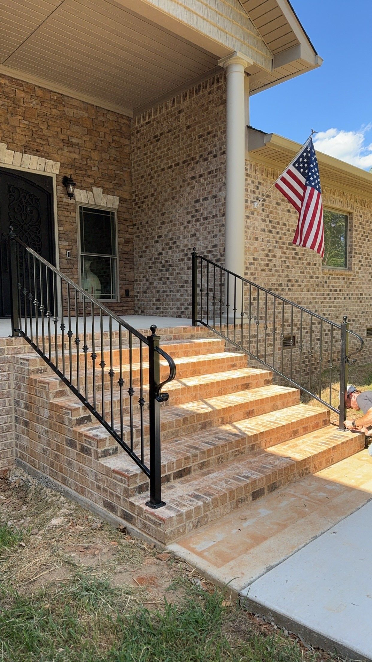 Brick house entrance with steps, black railings, and an American flag hanging by the porch.