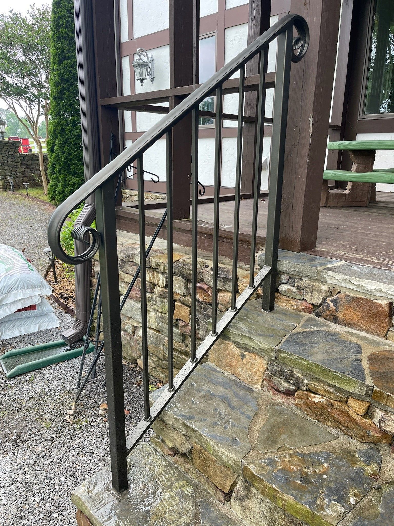 Black metal handrail and railing beside stone steps leading up to a house porch.
