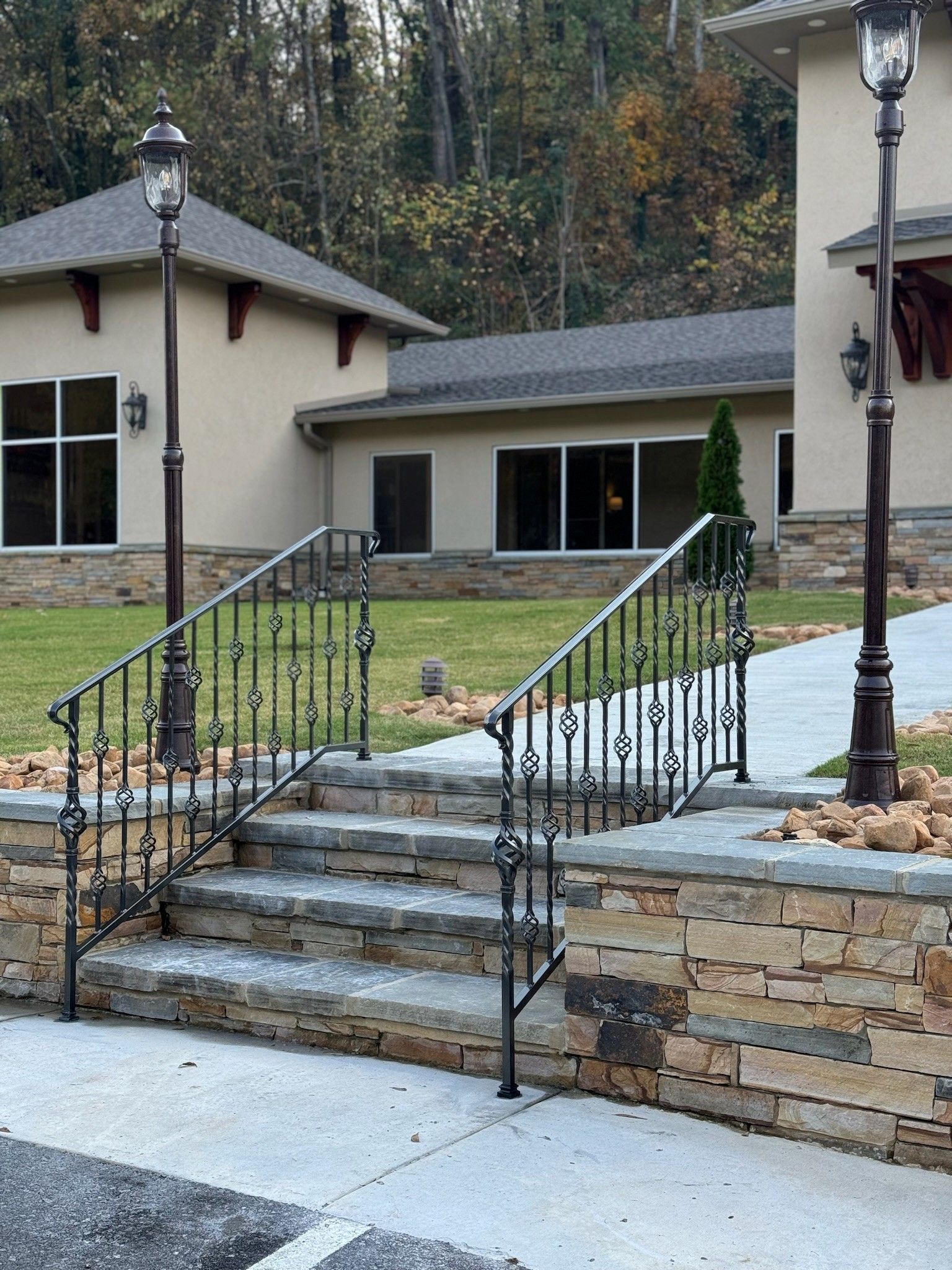 Stone front steps with black railings leading to a beige building entrance, with lampposts and landscaped walls.