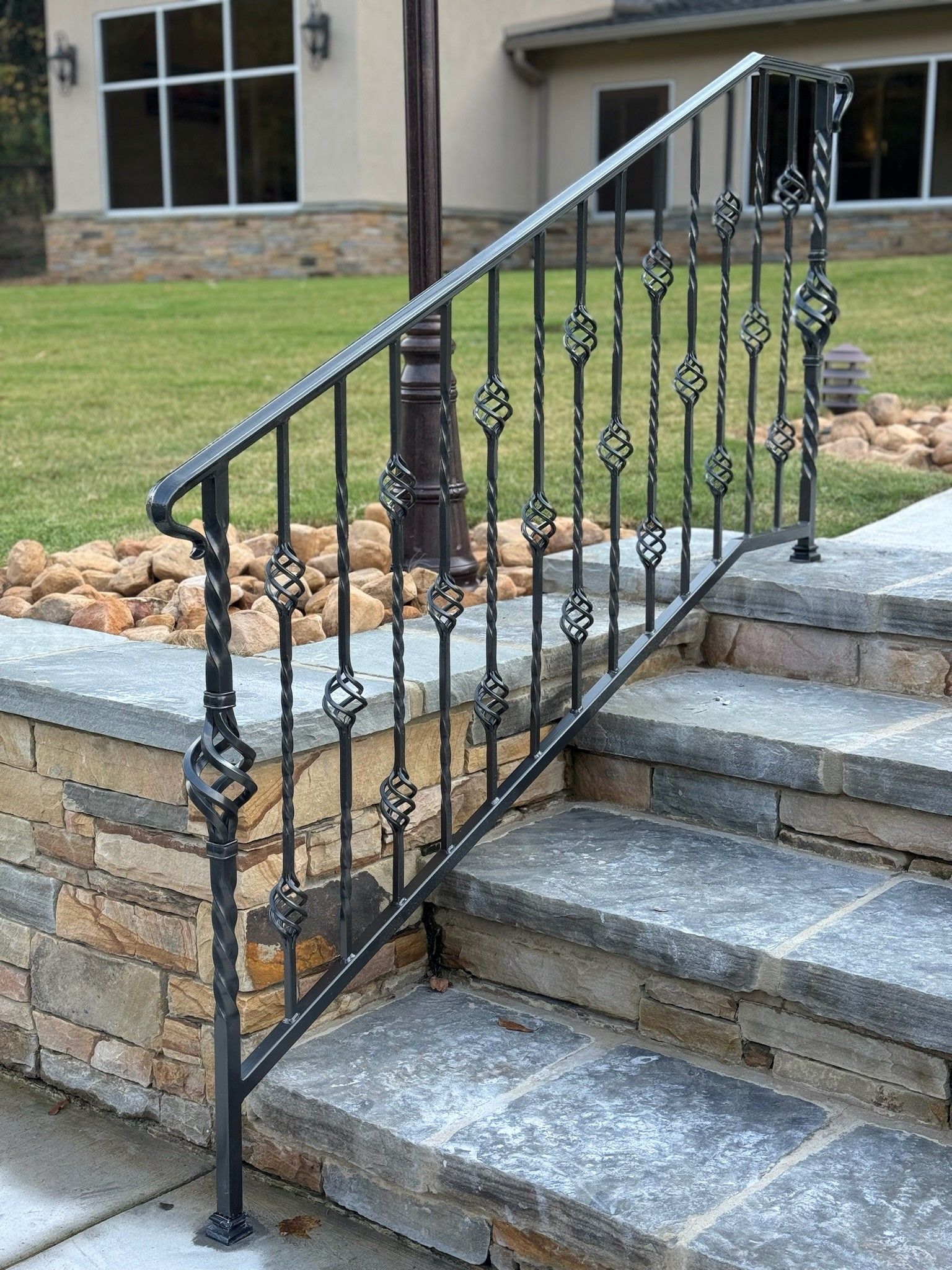 Black wrought-iron handrail along stone steps beside a brick-and-stone house entrance