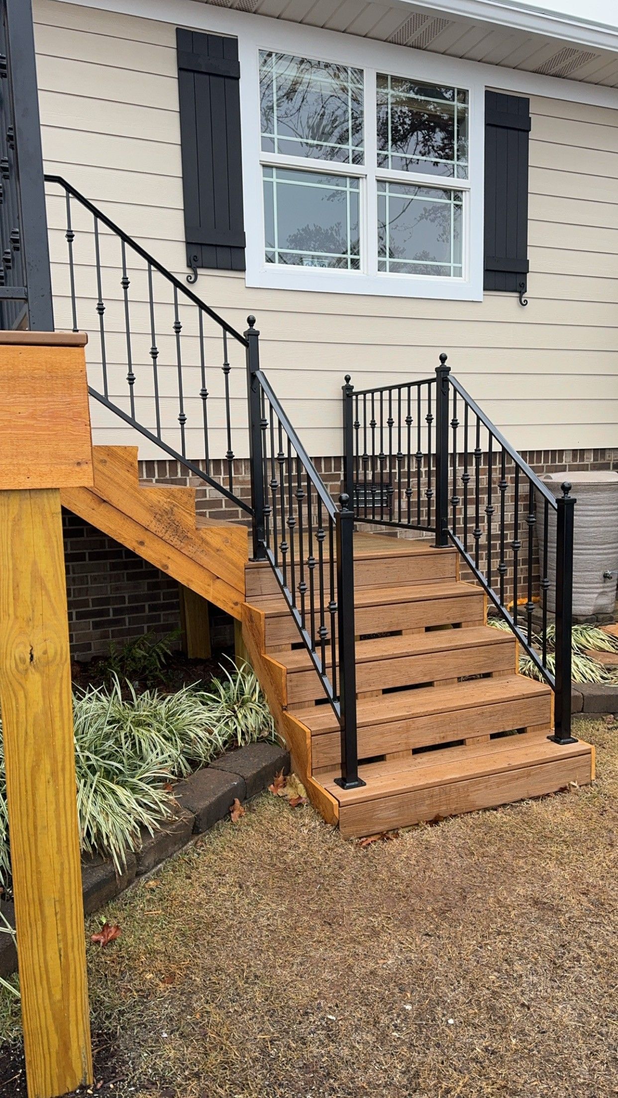 Front steps with black metal railings leading to a beige house with white-trimmed window and black shutters