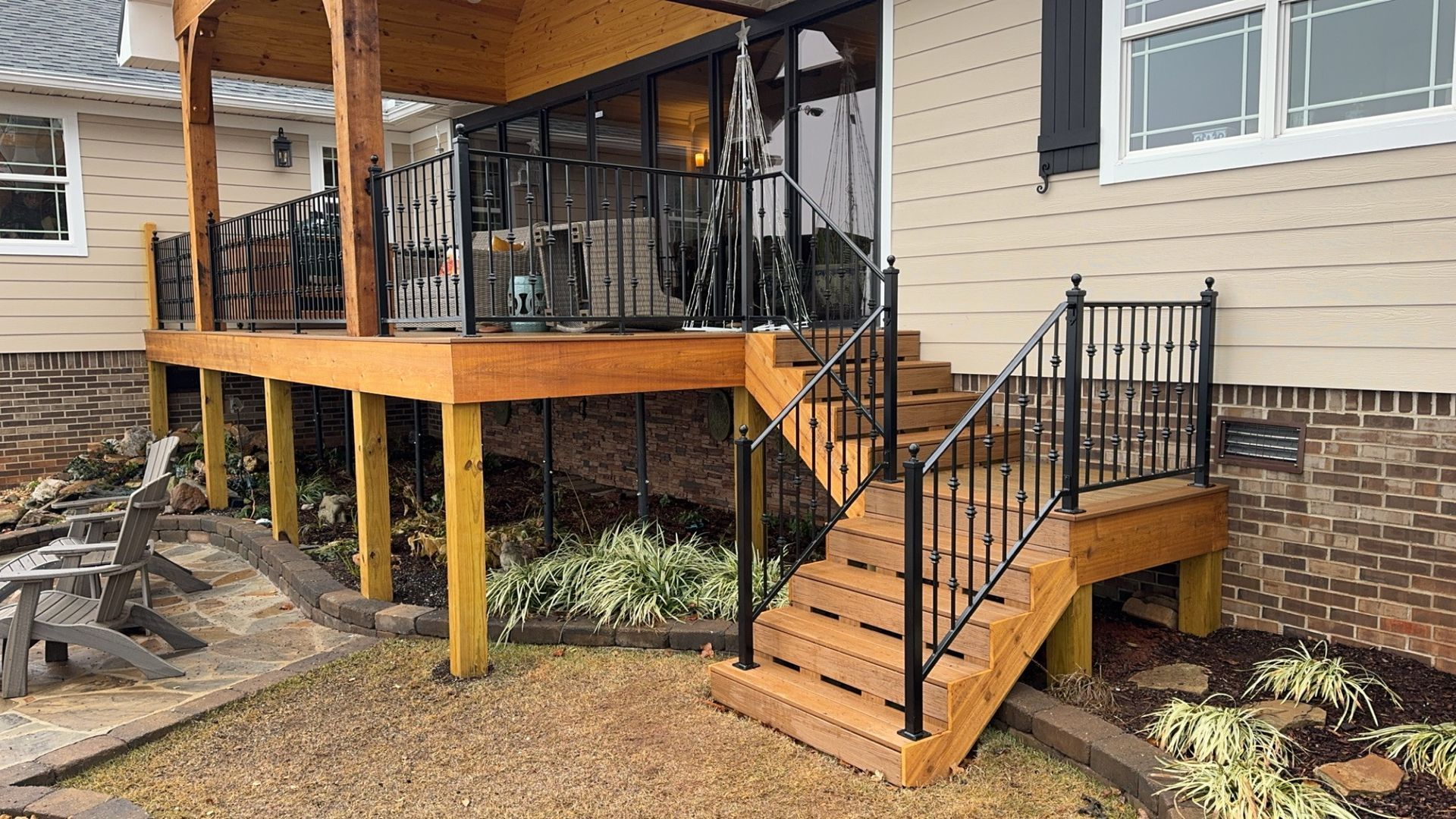 Wooden porch and stairs with black railings attached to a beige house over a gravel yard.