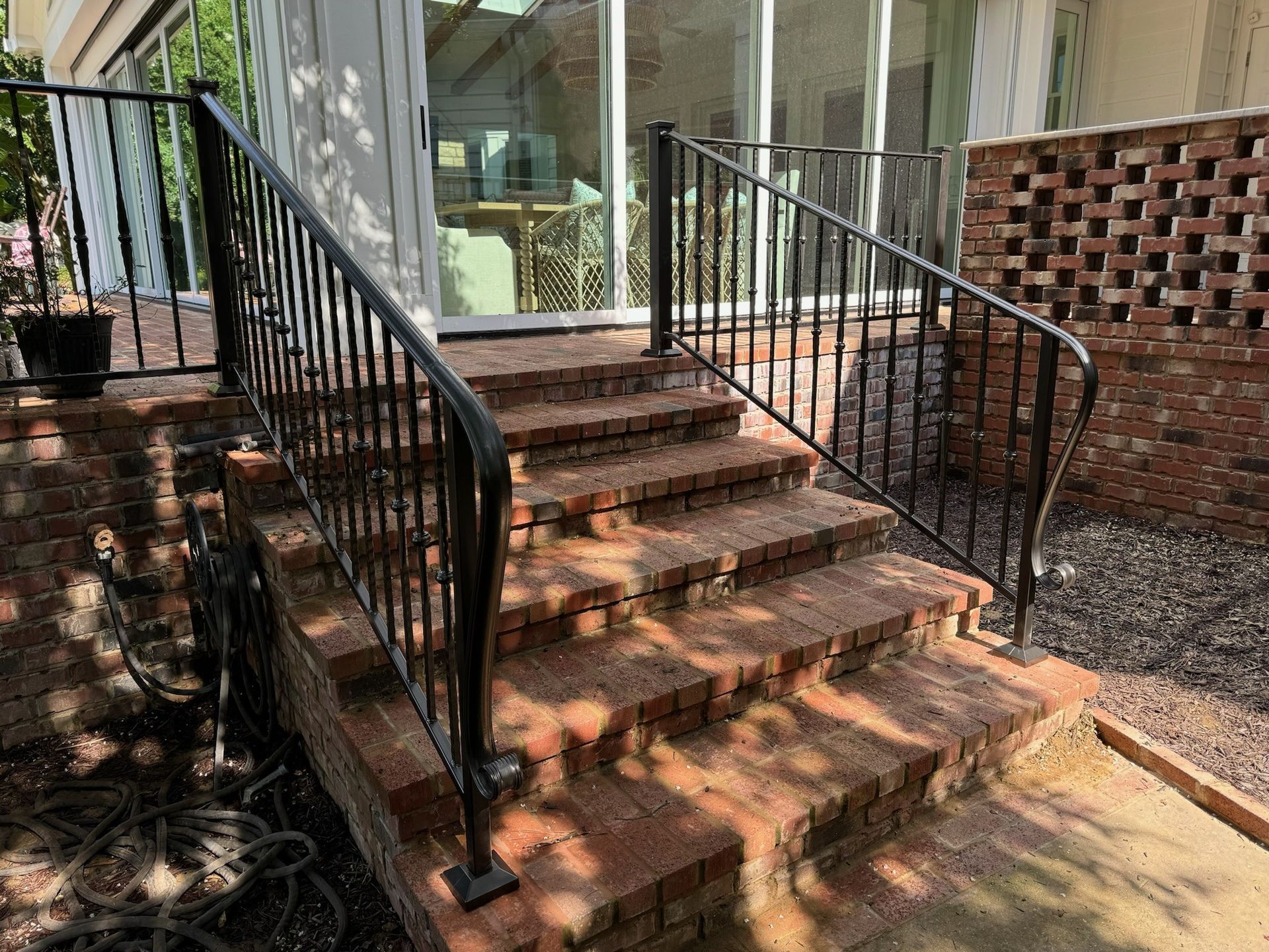 Brick front steps with black metal railings leading to a glass door entrance