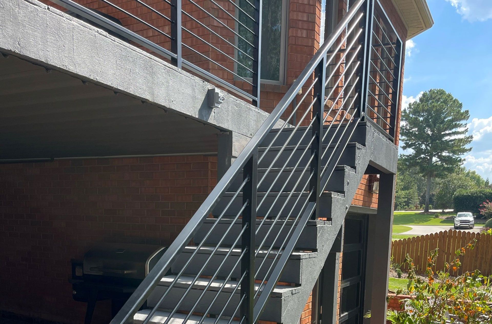 Exterior metal staircase beside a brick building, with a parked car and trees in the background