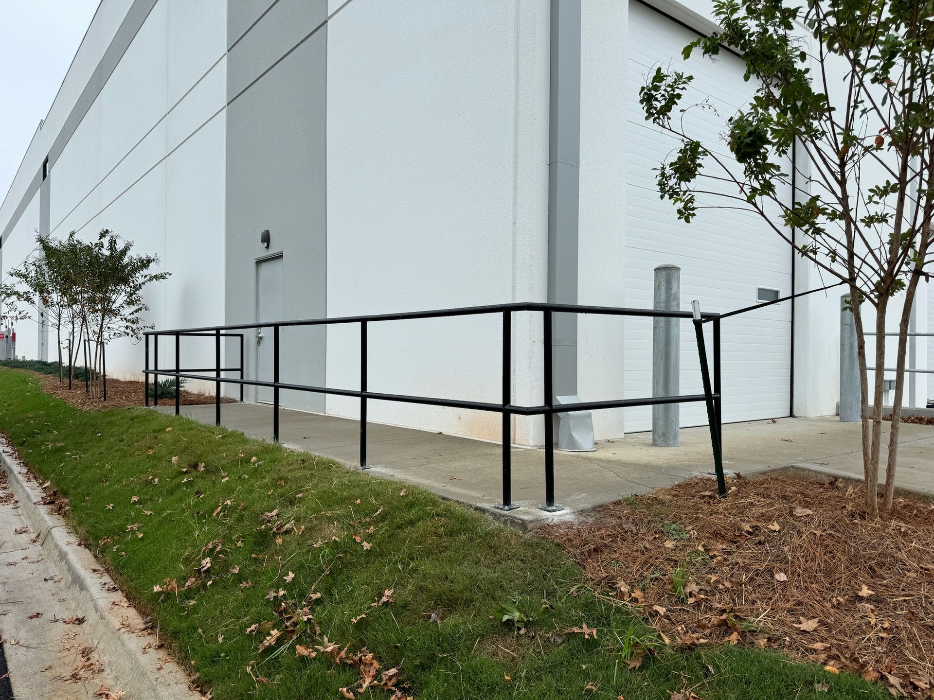 Exterior of a white building with a black handrail ramp and landscaped grass strip