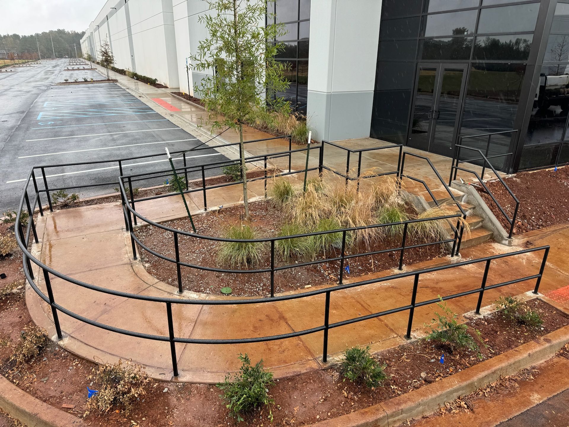 Accessible ramp beside a building entrance, with black railings and landscaped planters after rain