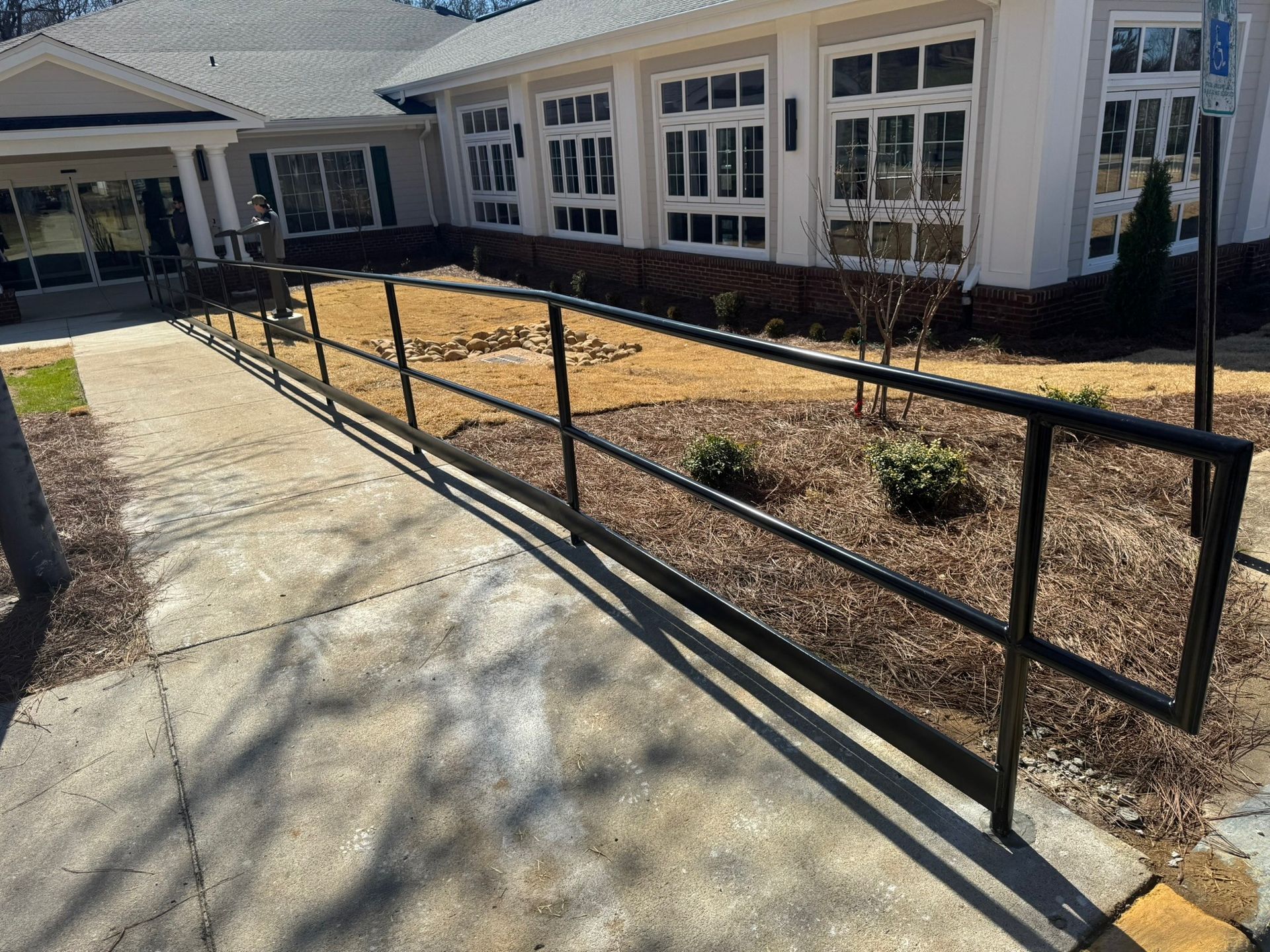 Black metal handrail along a concrete walkway beside a building with windows and a mulch bed