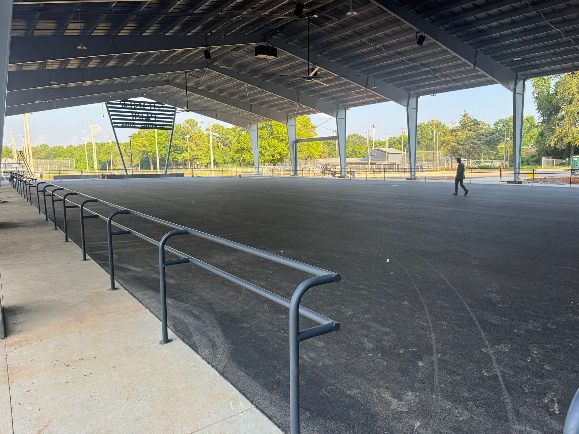 Covered outdoor skate park with railings and ramps, with one person standing in the distance.