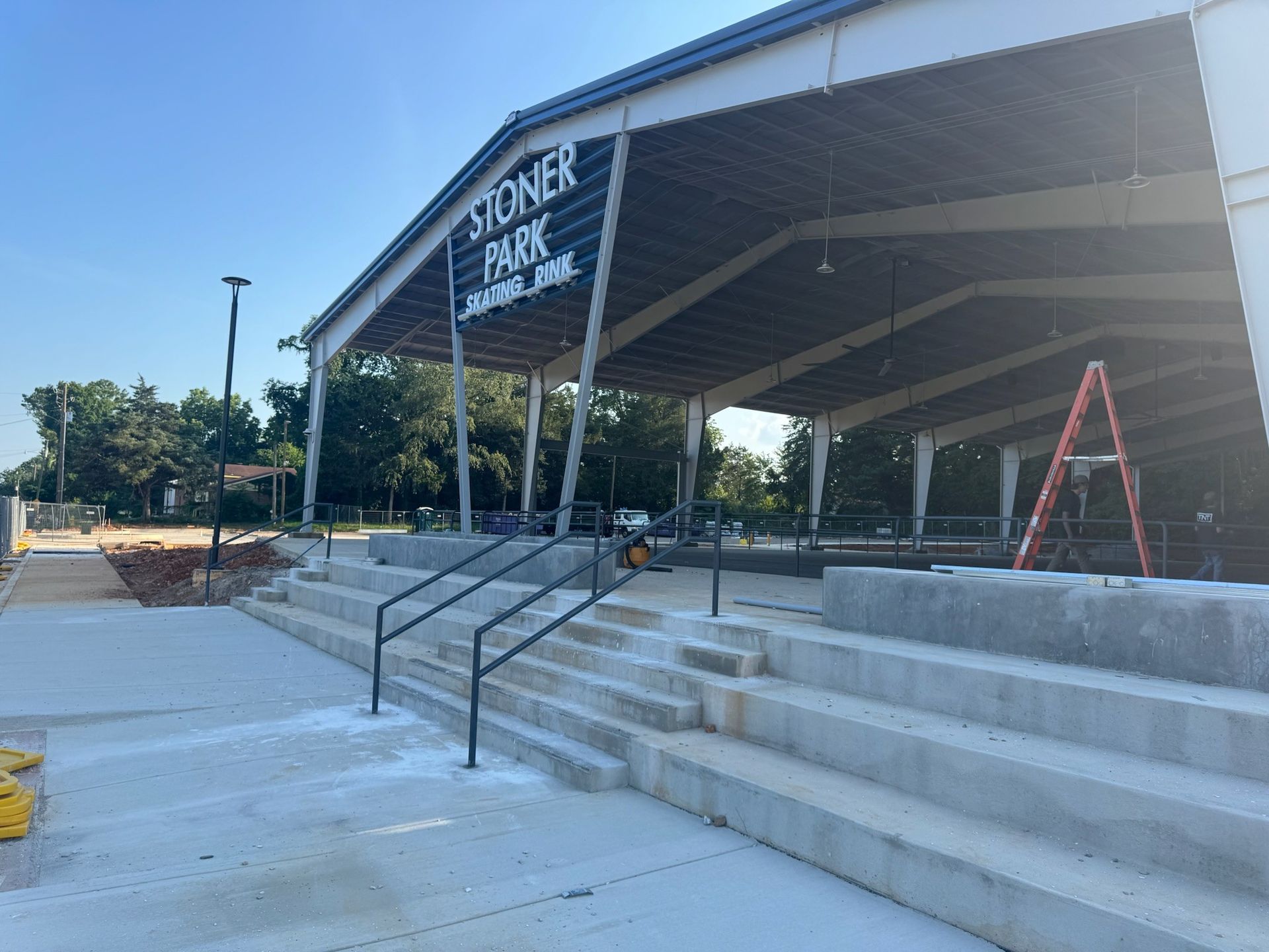 Outdoor covered stage labeled “Stoner Park” with concrete steps and ramp in a park setting