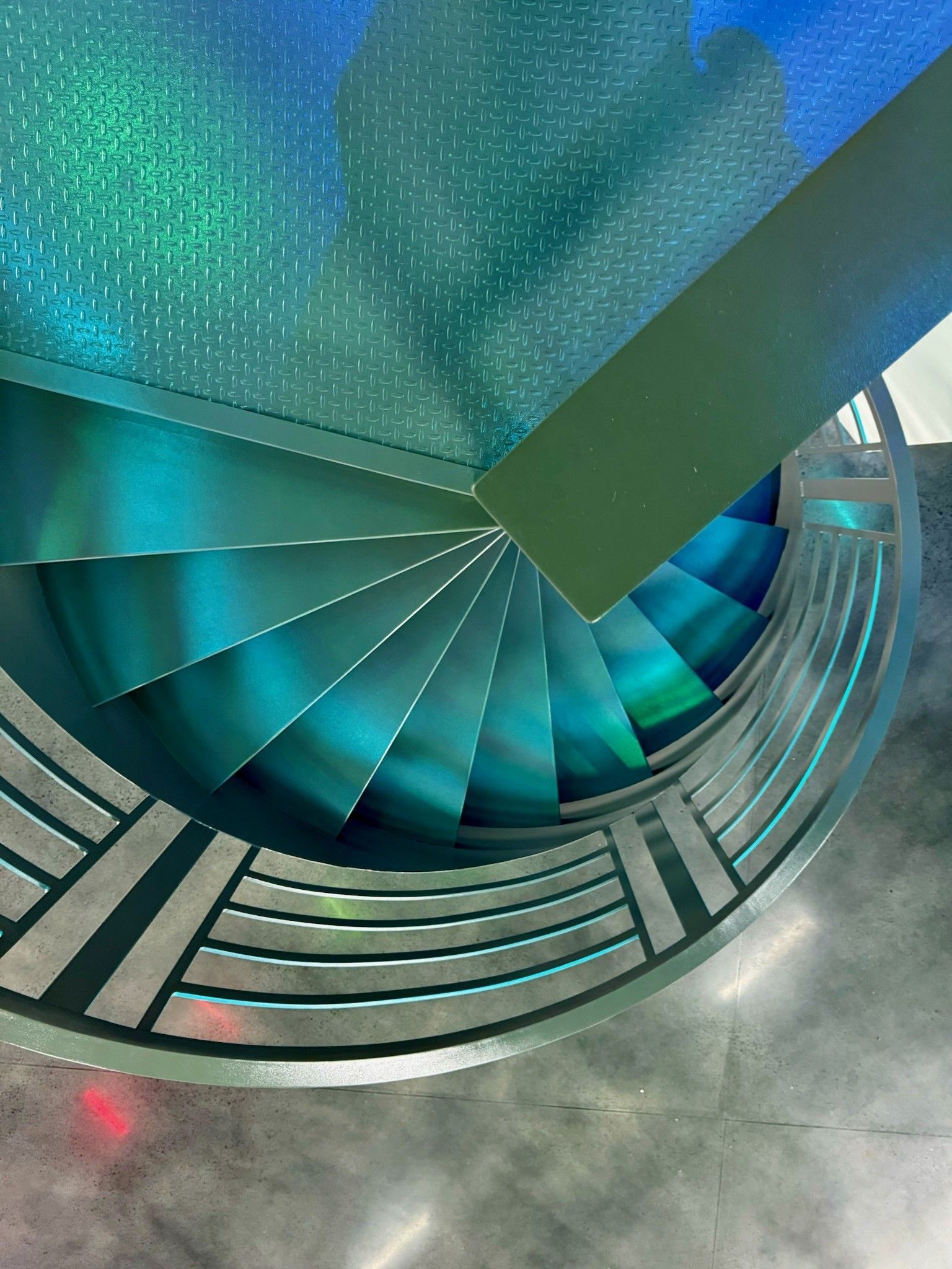 Spiral staircase with teal steps and metal railing inside a modern building