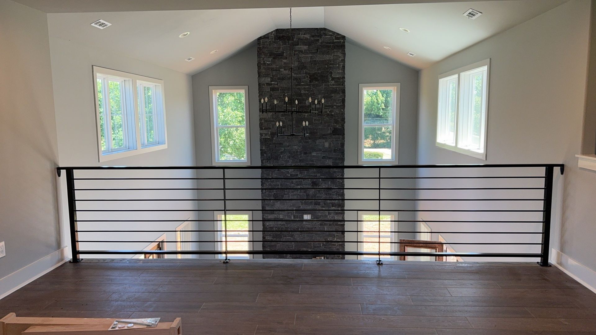 Interior loft walkway with dark wood floor, black railing, windows, and a central stone fireplace chimney