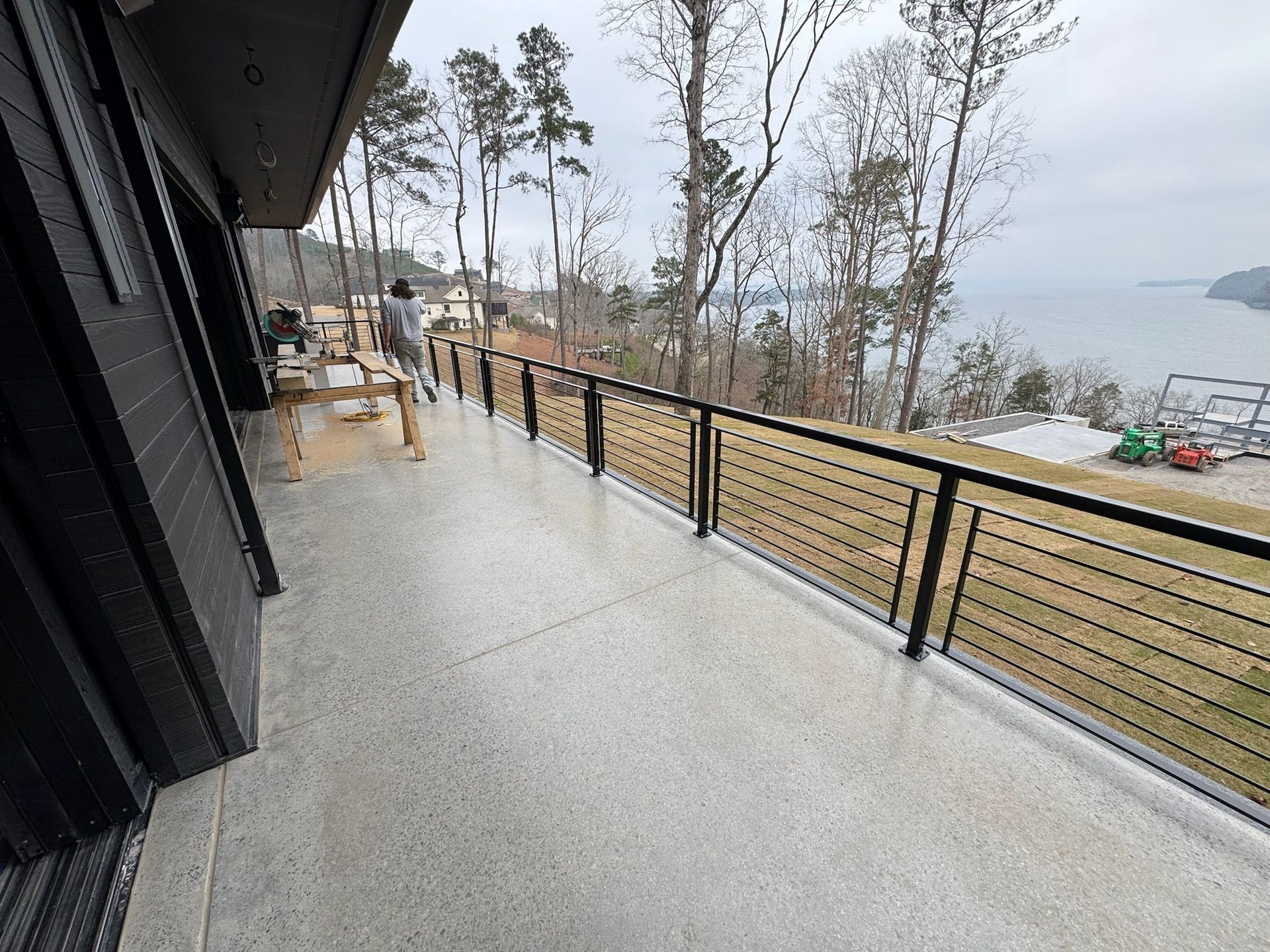 Deck overlooking a lake with black railing, wet floor, and trees along the shoreline