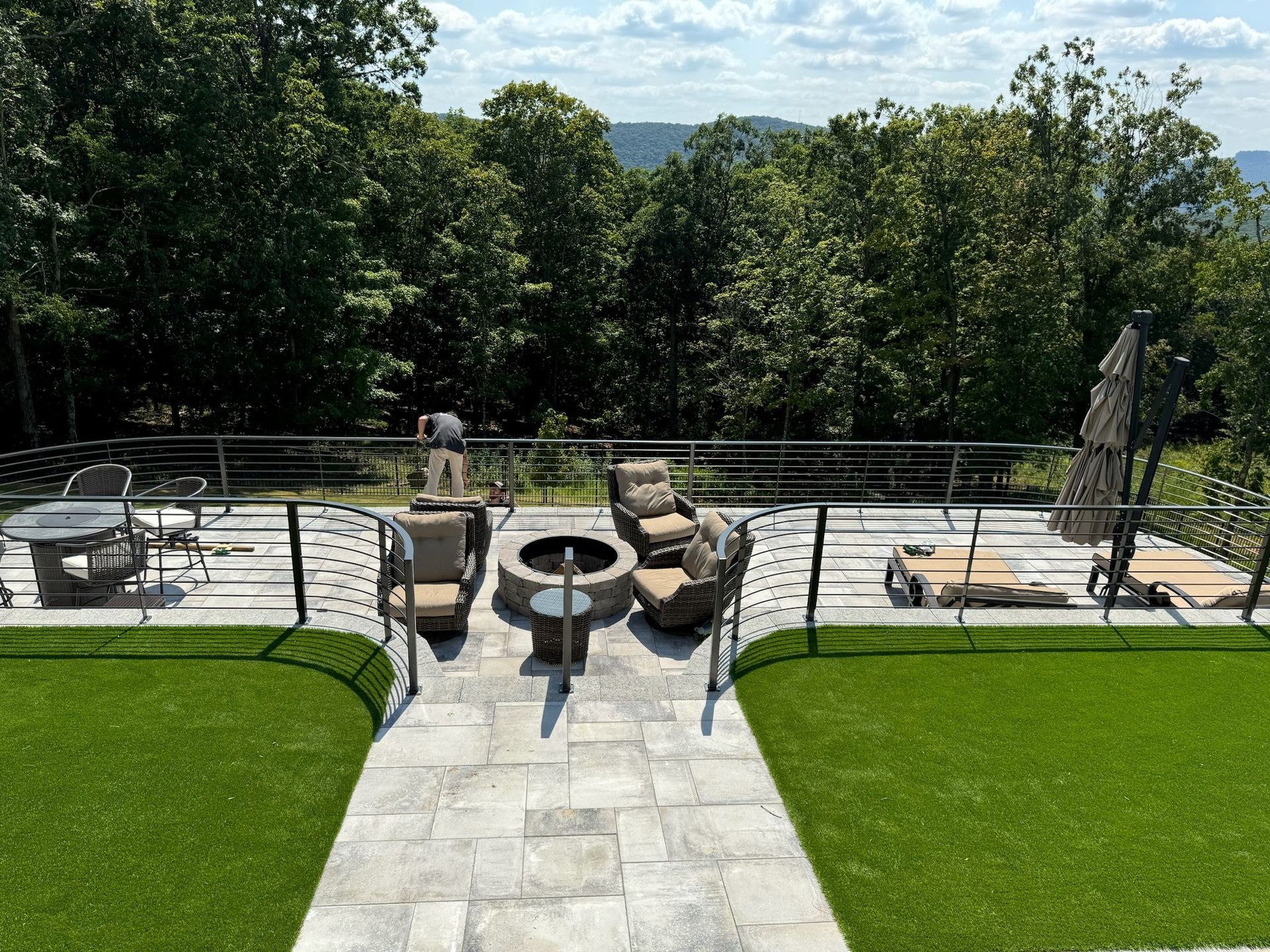 Patio terrace with outdoor seating, fire pit, umbrella, and manicured lawn overlooking trees and hills