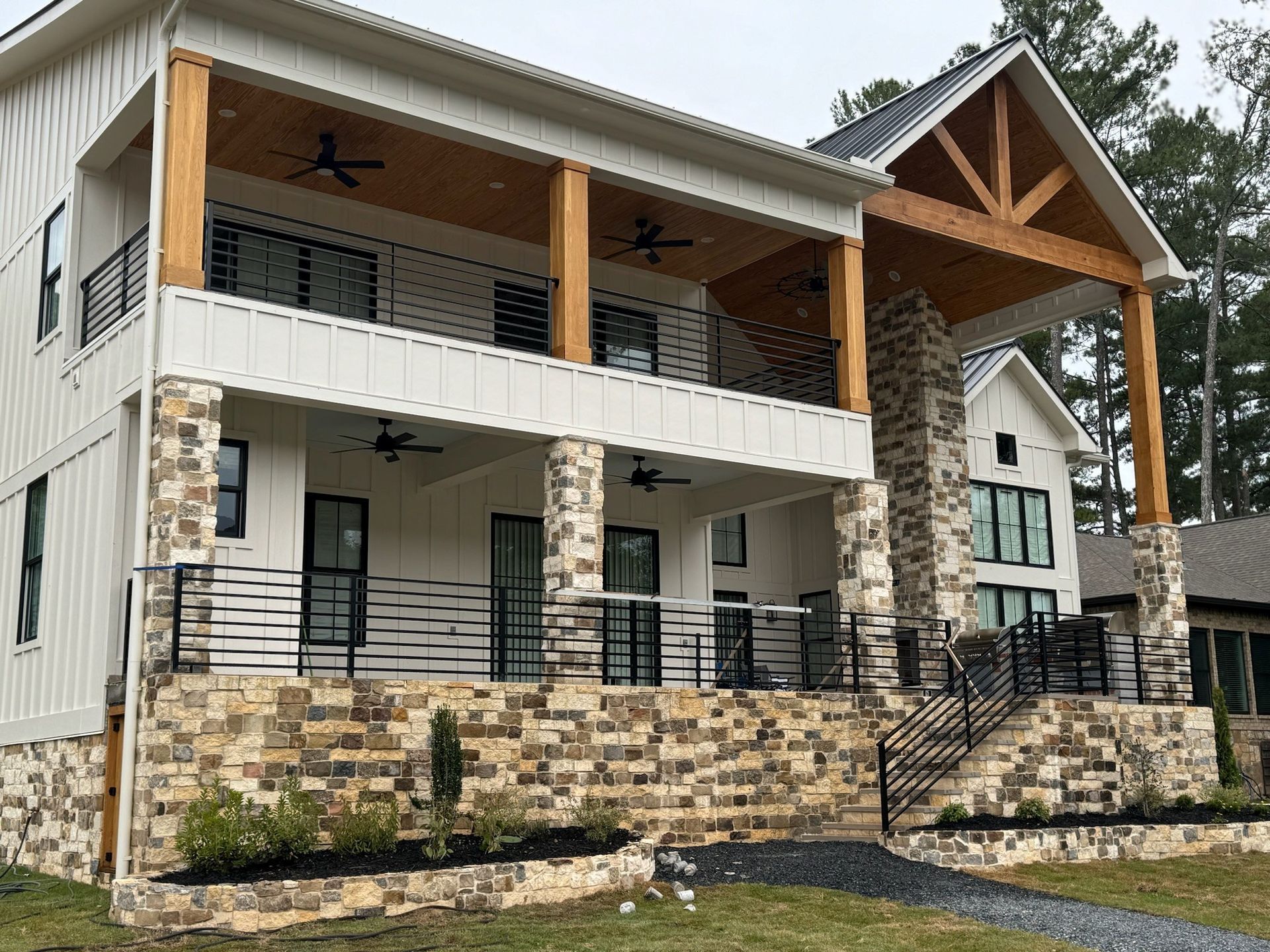 Two-story modern house with stone accents, covered porch, and balcony on a landscaped lot