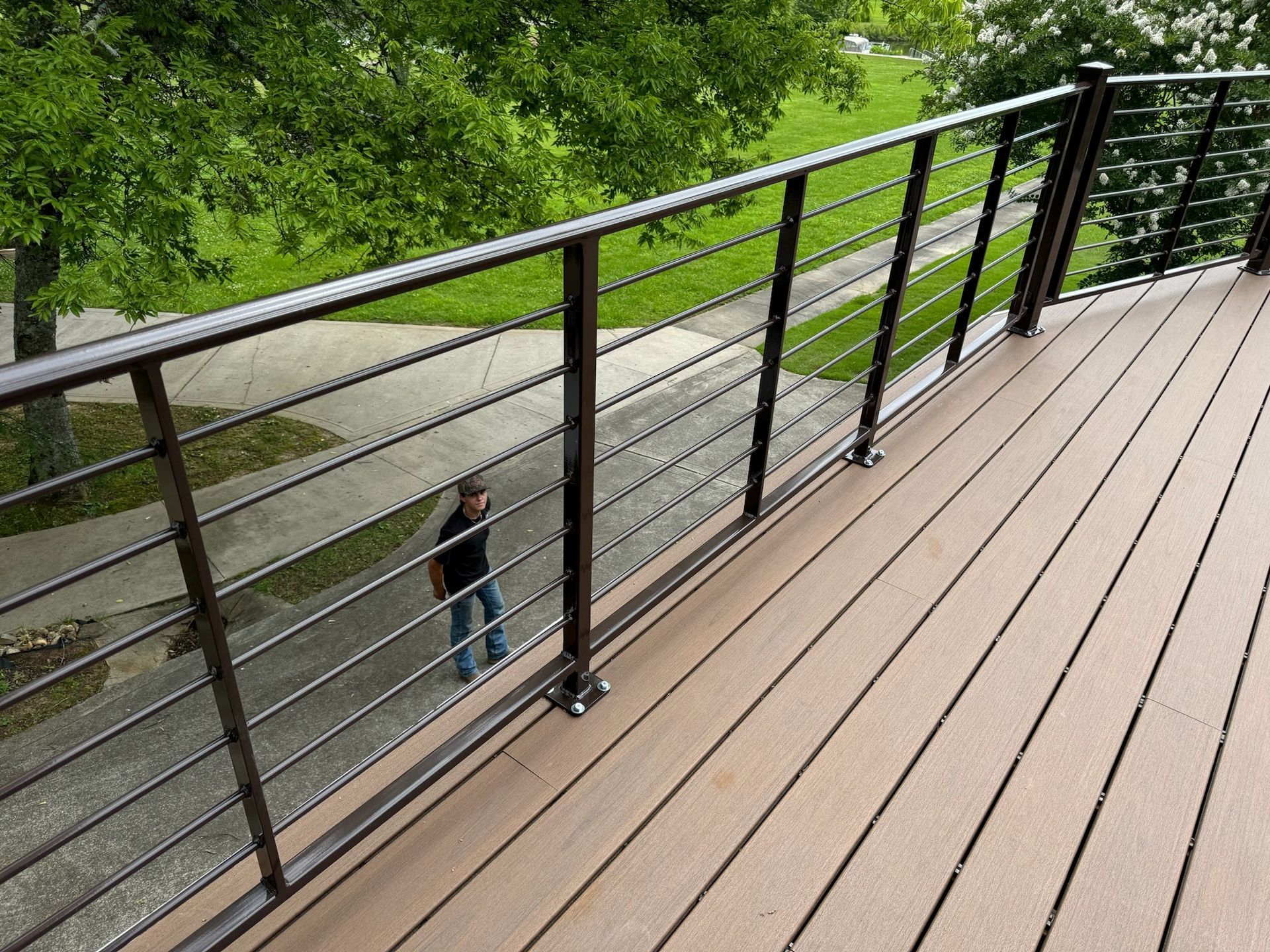 Wooden deck with black railing overlooking a tree-lined path below