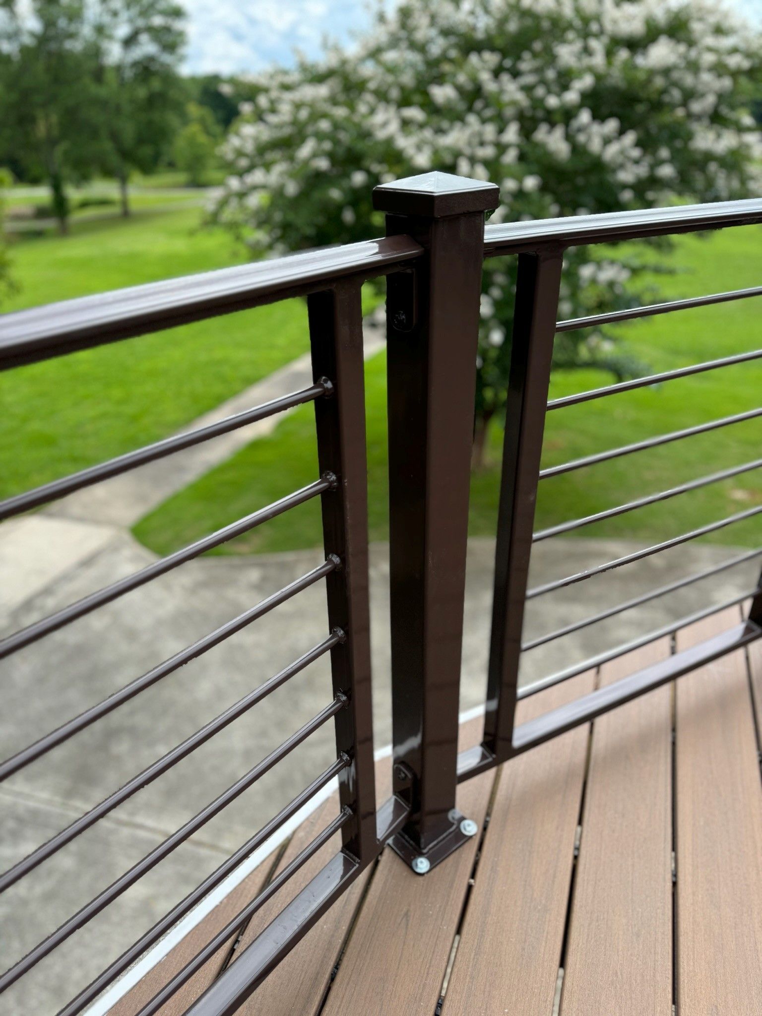 Dark brown cable railing on a wooden deck overlooking a green yard and flowering tree.