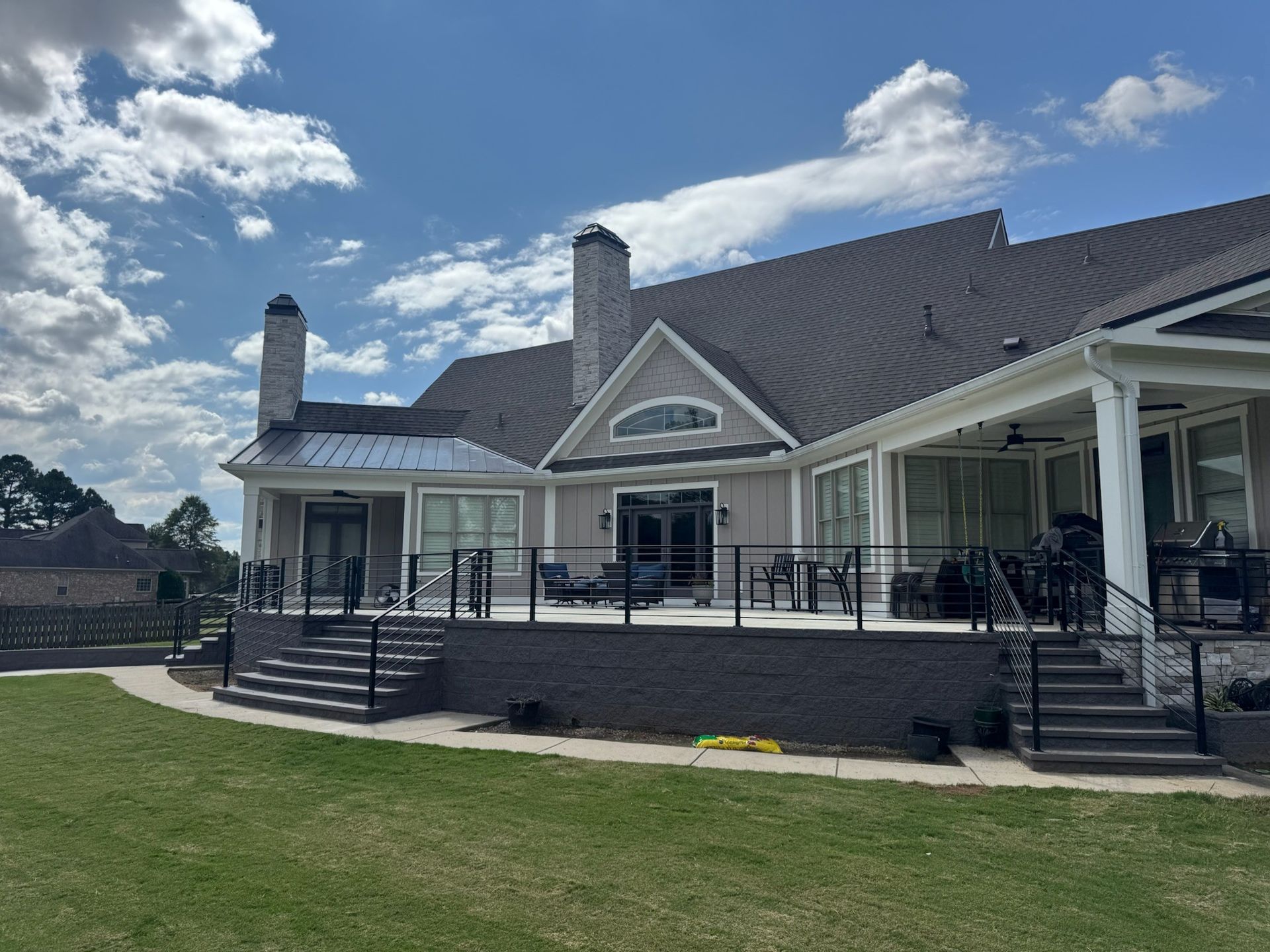 Large white house with a dark roof, porch railings, and steps, set on a green lawn under a partly cloudy sky