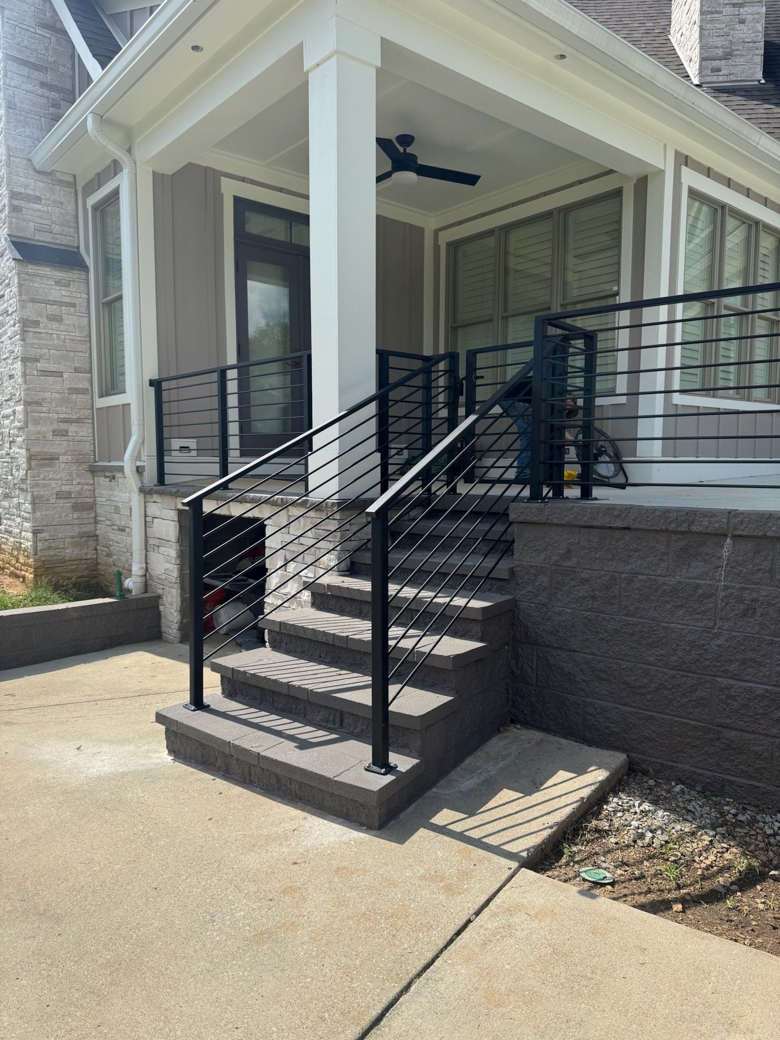 Front porch with black metal railing and stairs leading to a house entrance, with an accessibility ramp beside it