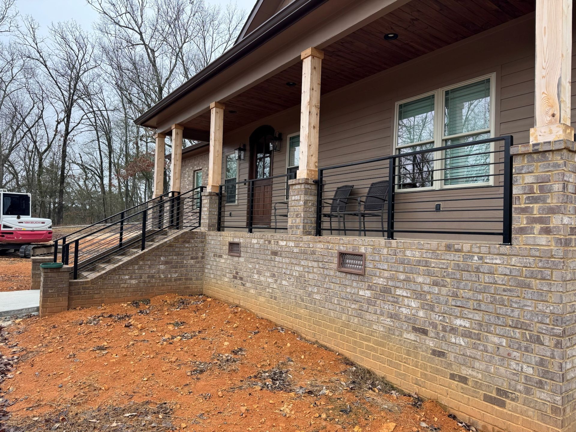 Brick house porch with stone retaining wall, wooden posts, and a gravel driveway on a cloudy day