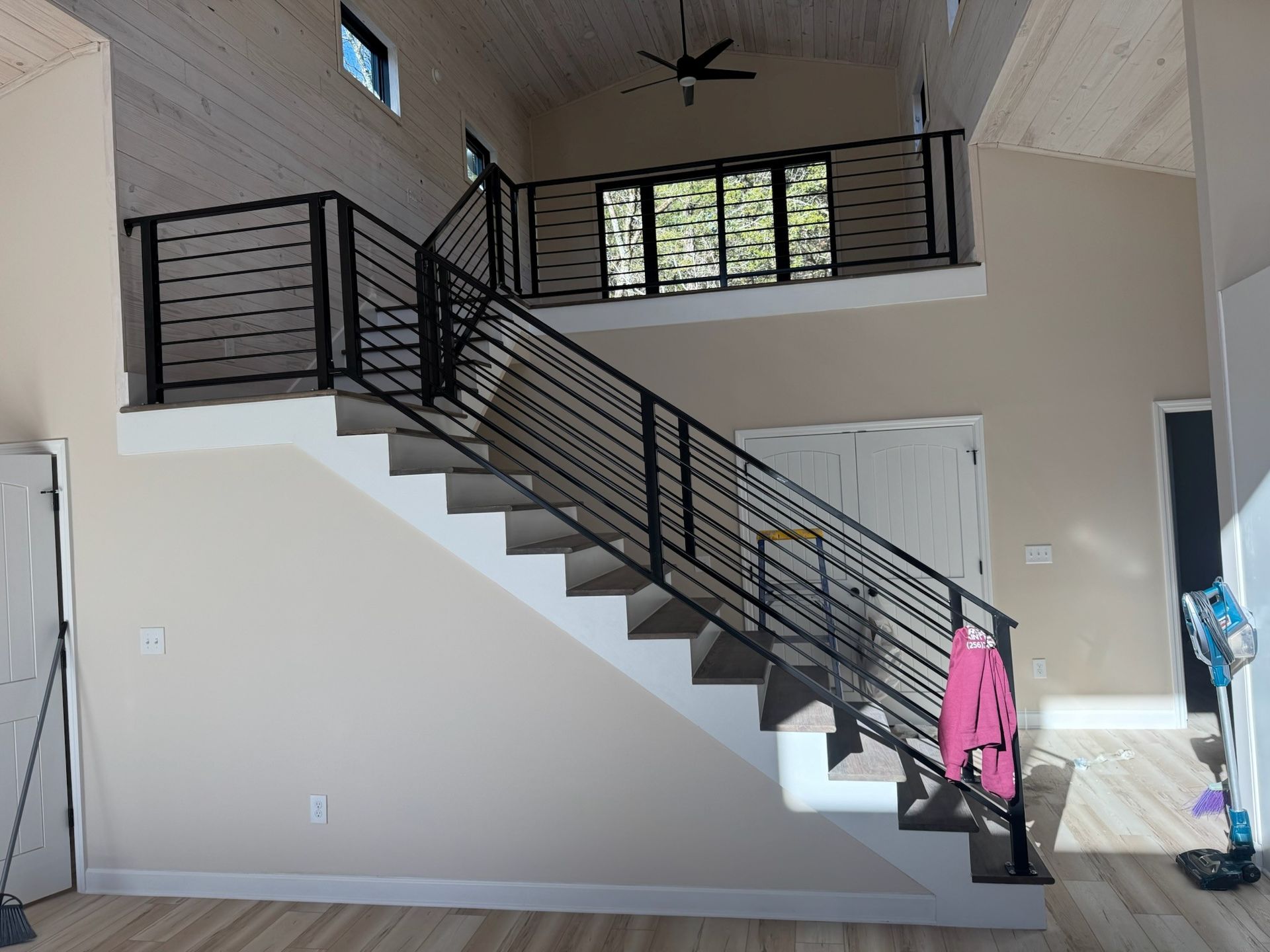Indoor staircase with black railing, white walls, and a pink item hanging on the banister