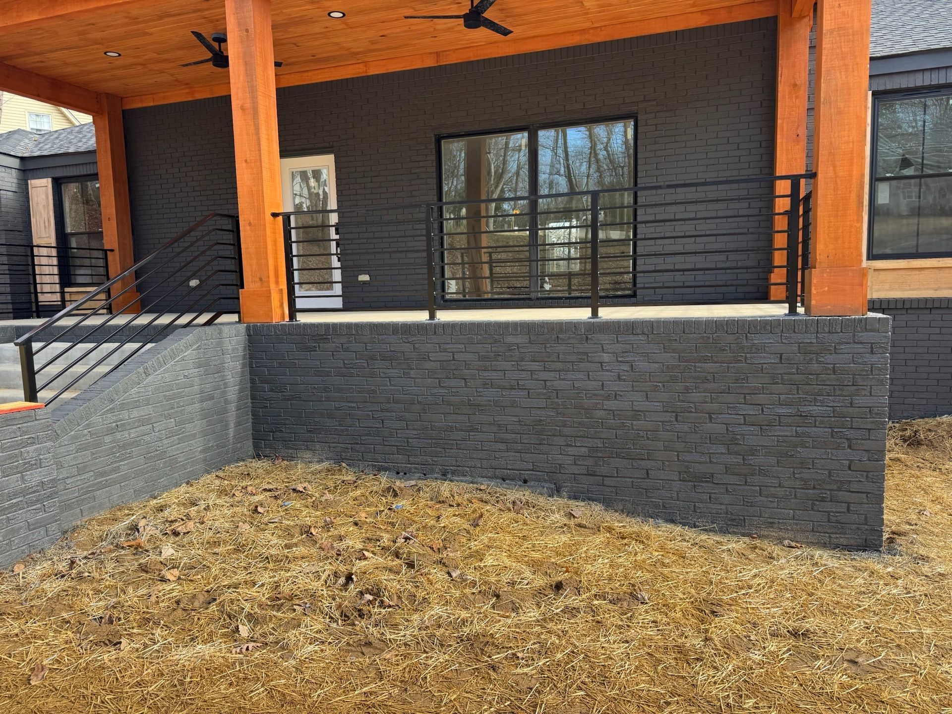 Covered patio with orange beams, dark brick walls, and a mulch-covered yard in front