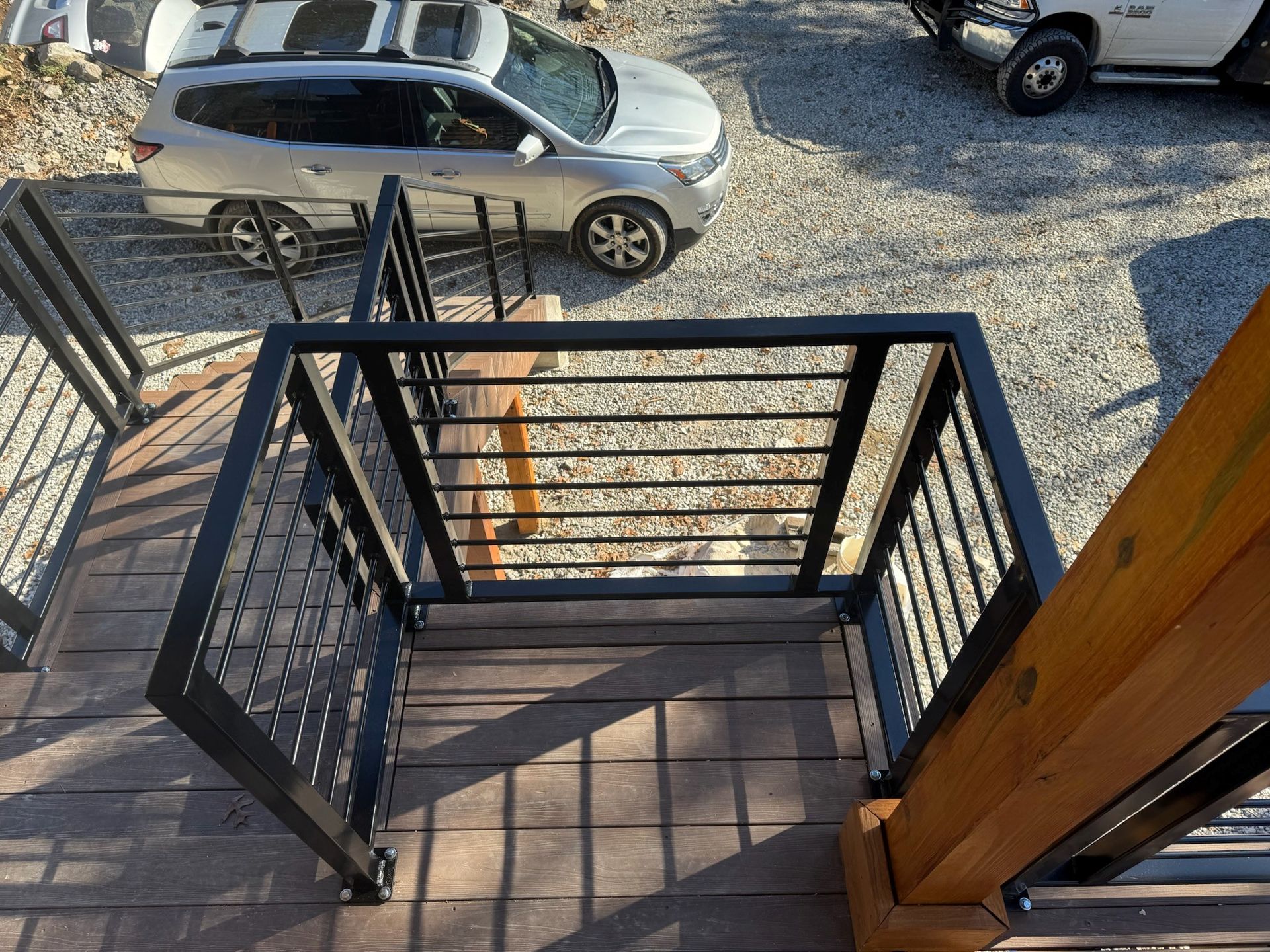 Top-down view from a black metal balcony staircase to a gravel lot with a silver SUV and other vehicles below.
