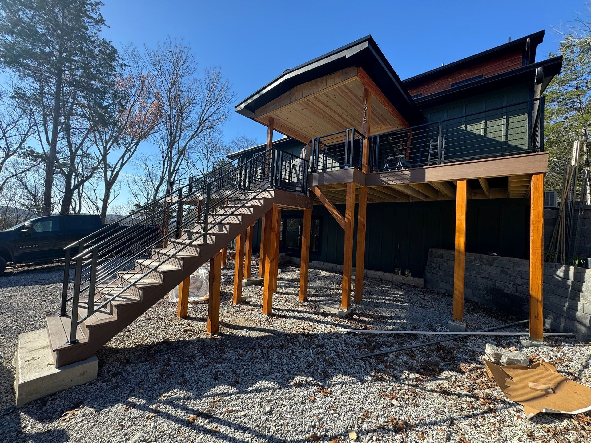 Stilted house with exterior stairs on a gravel lot under a clear blue sky