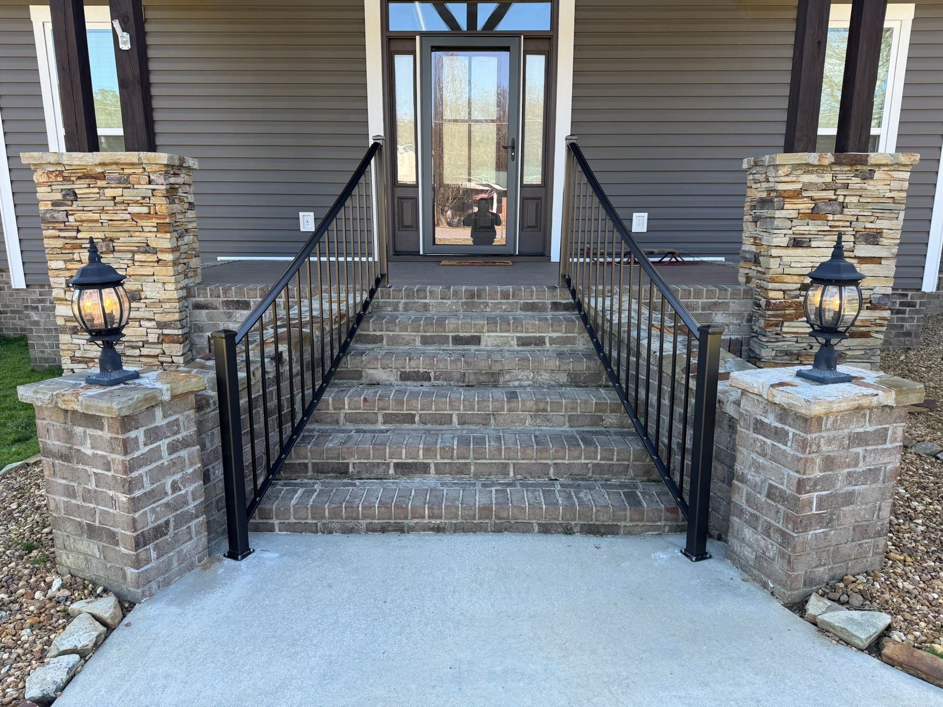 Front entrance with brick steps, black railings, and lanterns leading to a glass door.