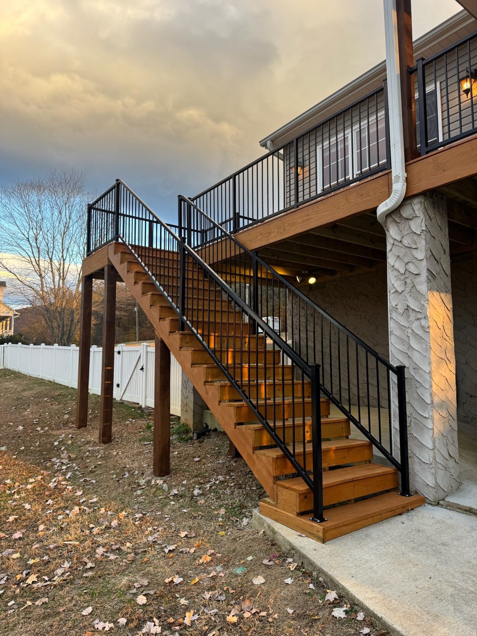 Outdoor wooden staircase with black railings leading to an elevated deck on a modern house in fall.