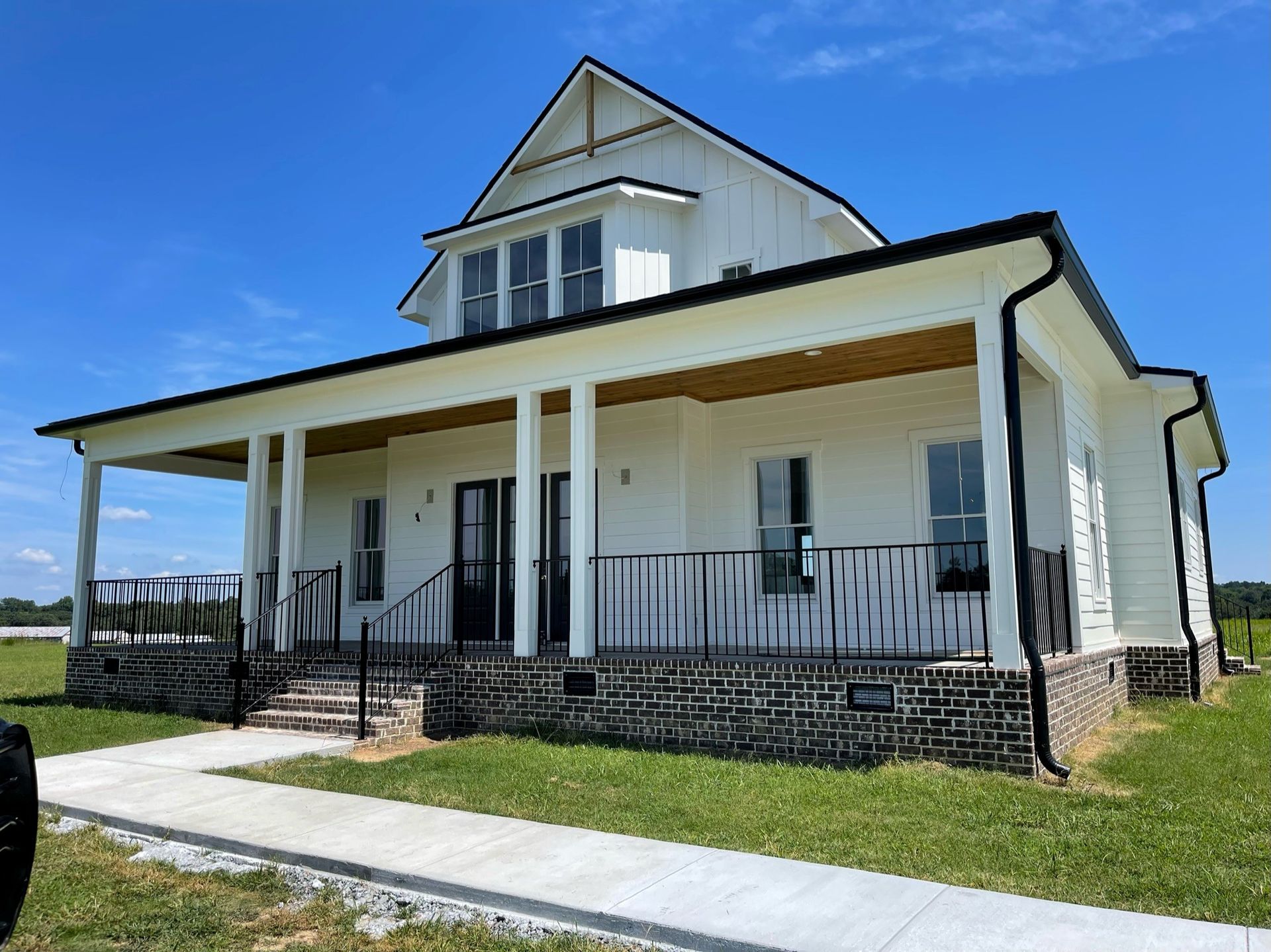 White farmhouse with a covered porch and black metal railing under a blue sky