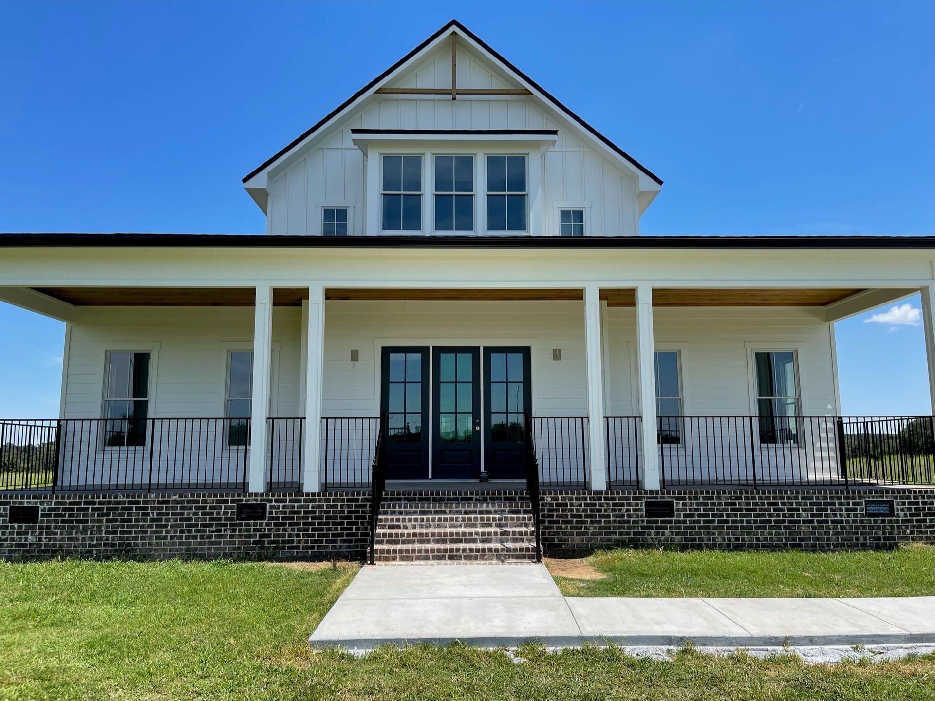 White house with a wide front porch, central steps, and a green lawn under a blue sky