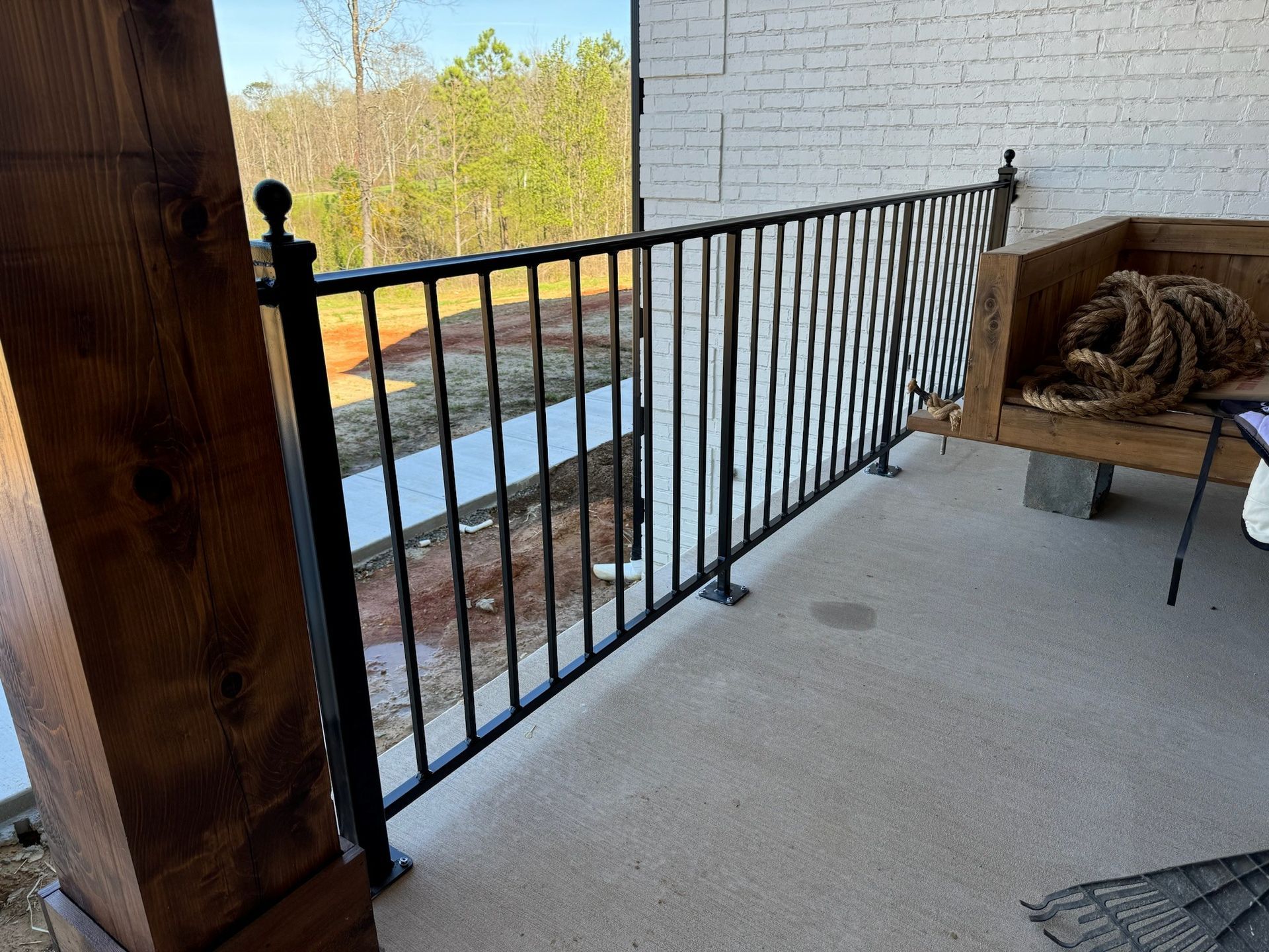 Covered balcony with black metal railing, white brick wall, and a wicker chair with cushions.