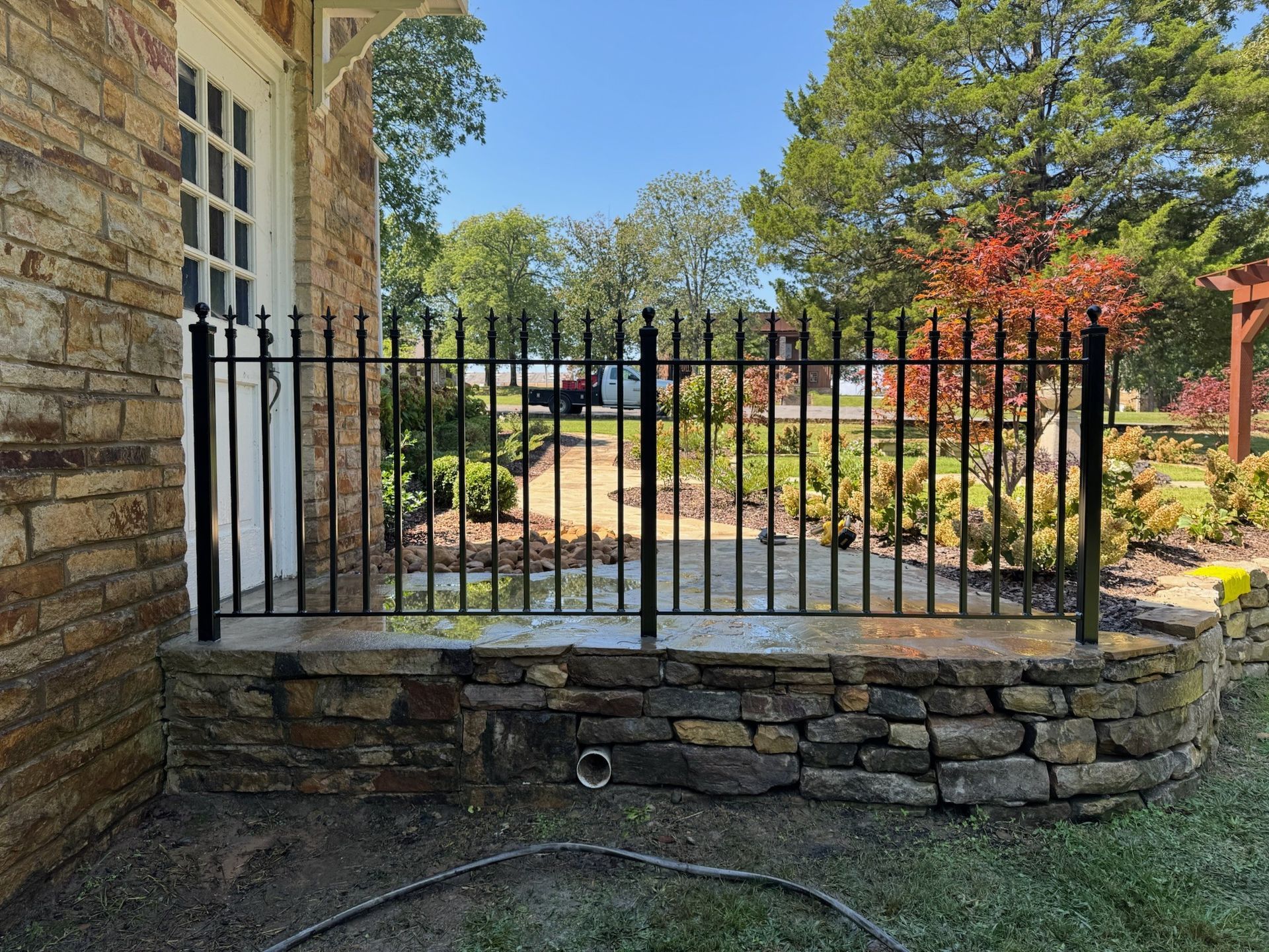 Stone wall with black iron fence in front of a house and garden walkway