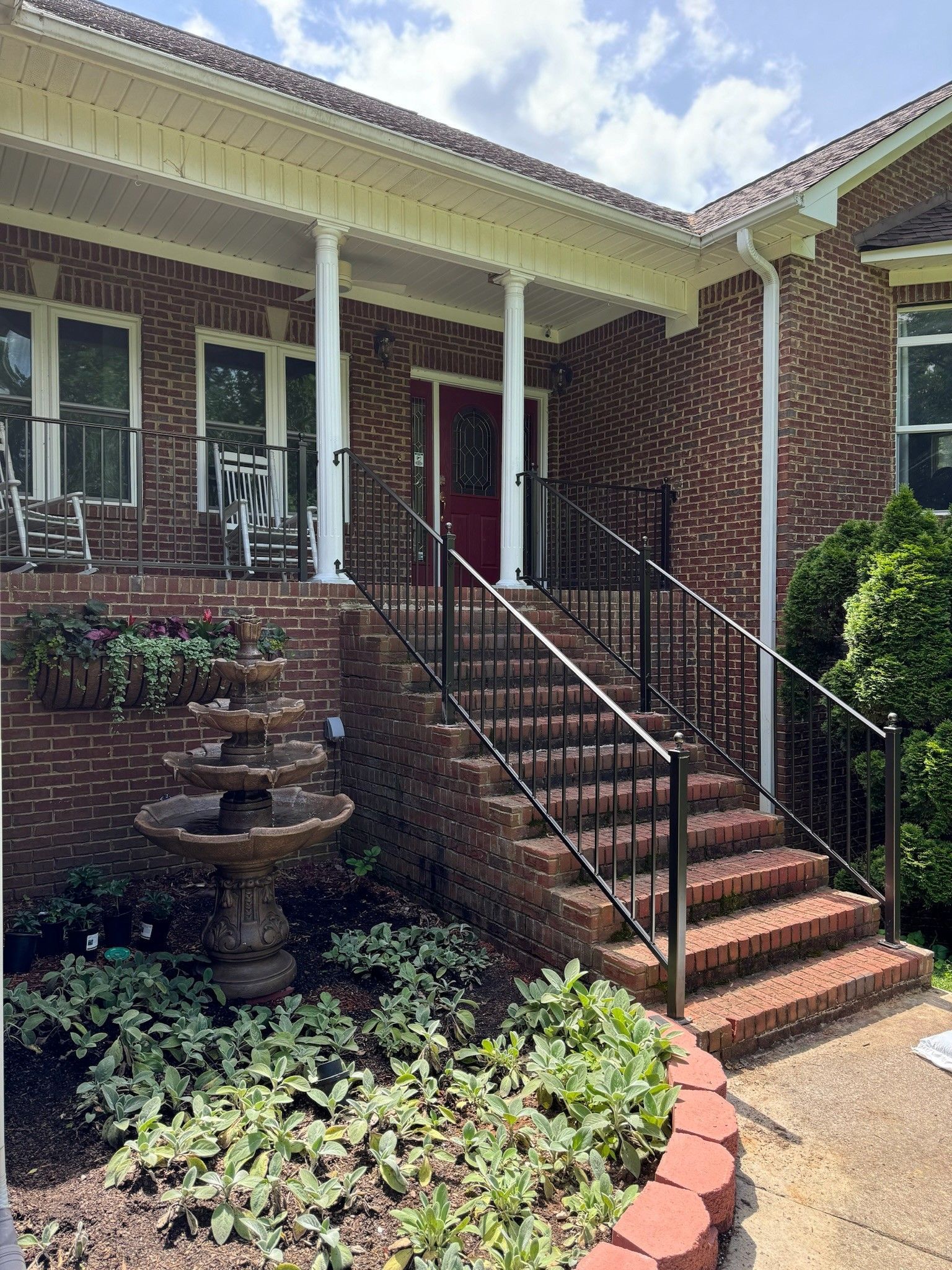 Brick house front entrance with steps, black railings, and a small garden and fountain