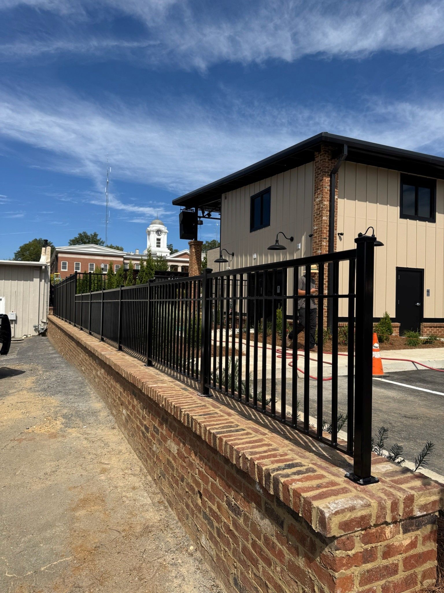 Brick-and-black metal fence beside a gravel driveway under a blue sky