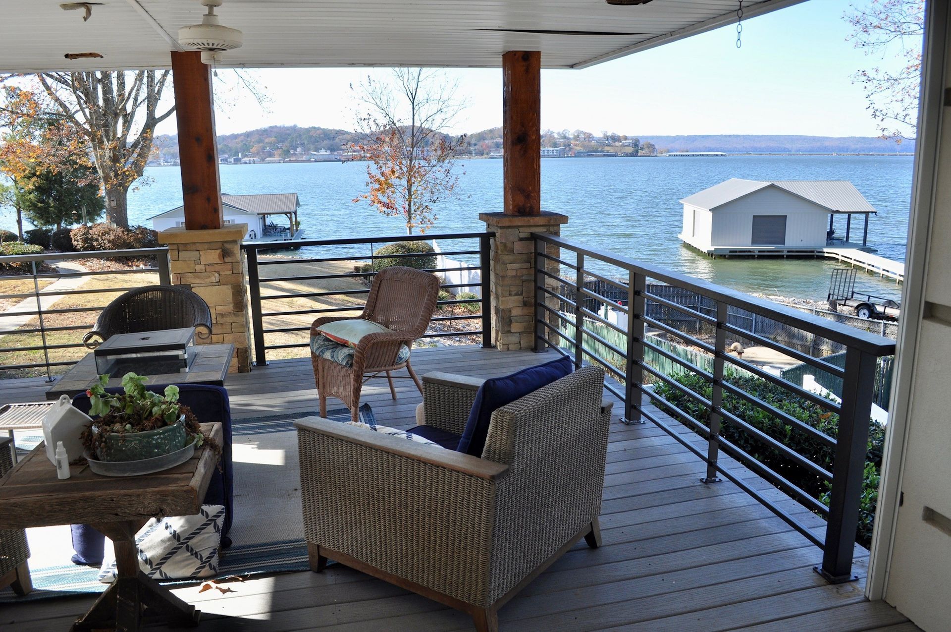 Covered lakeside deck with wicker chairs, grill, and a view of the water and boathouse