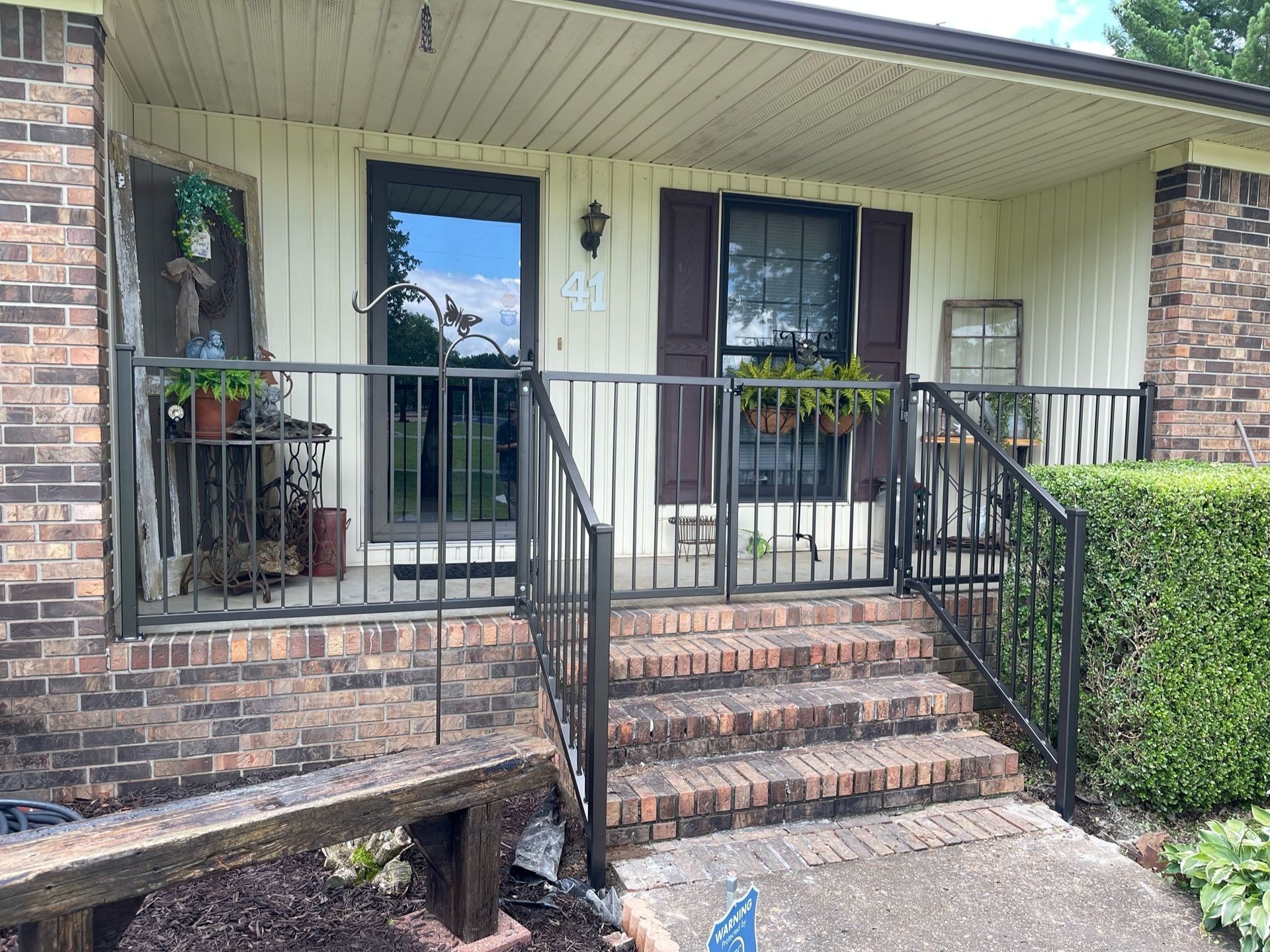 Front porch with brick steps, black railings, and beige siding on a small house