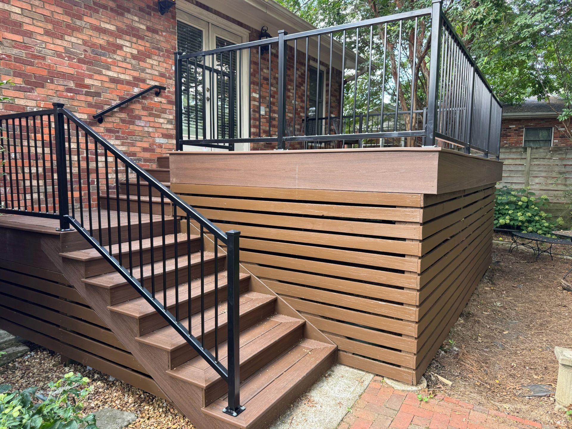 Backyard deck with stairs, black railing, and wood siding next to a brick house