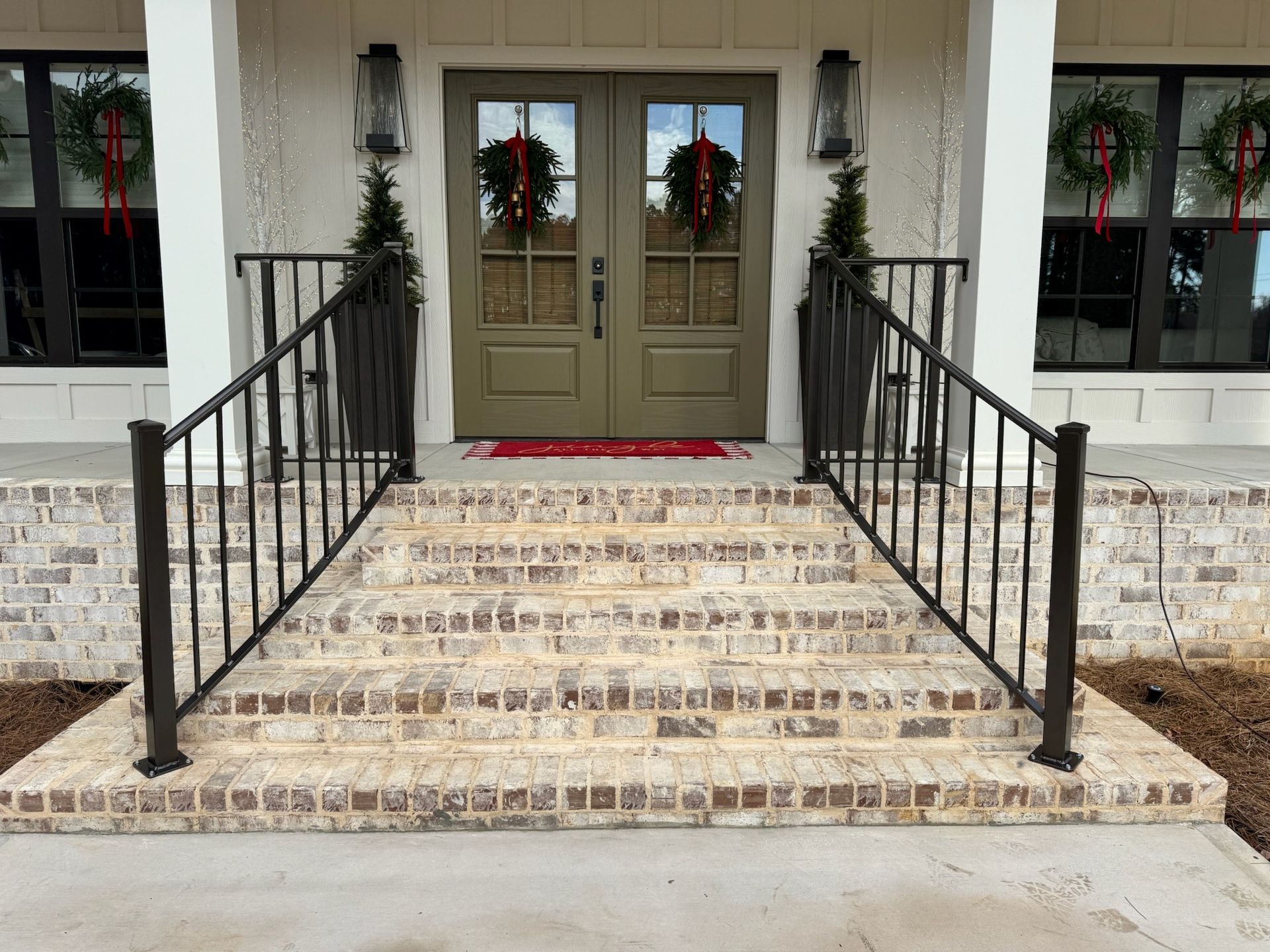 Front steps leading to double doors with wreaths, flanked by black railings and windows.
