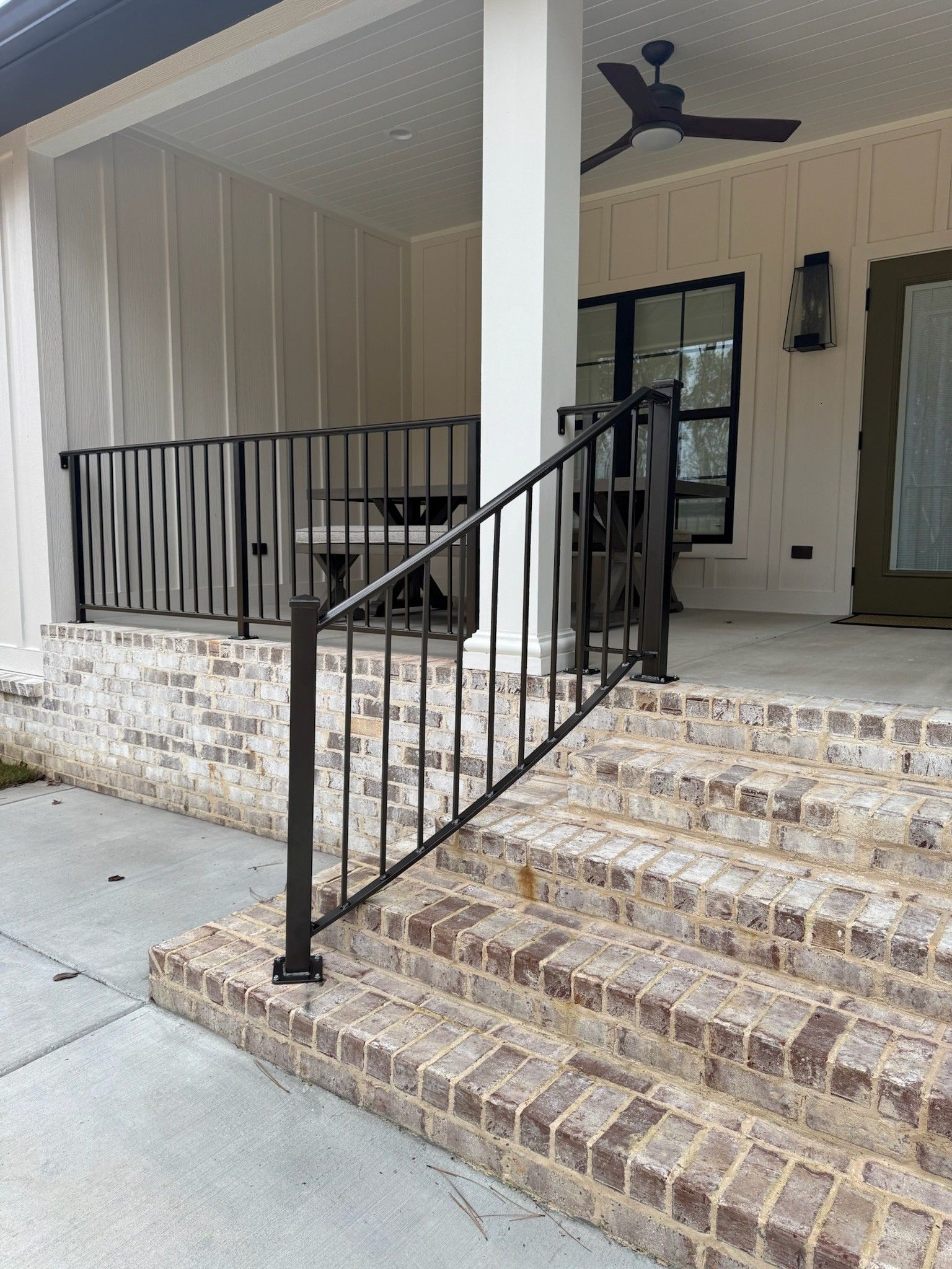 Front porch with brick steps, black metal railings, and a covered entrance to a beige house.