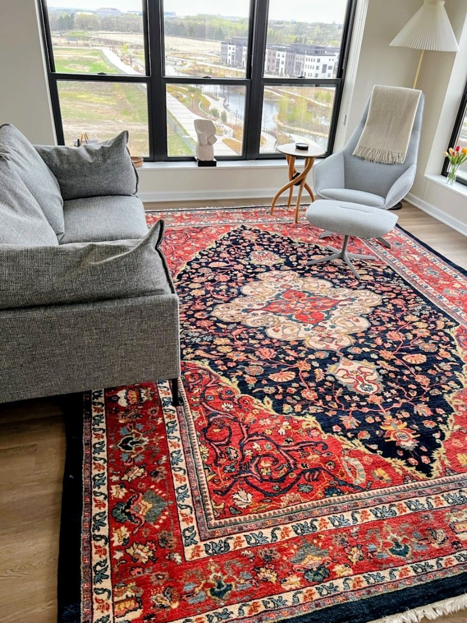 Living room with red and blue patterned rug, gray sofa, chair, and large window.
