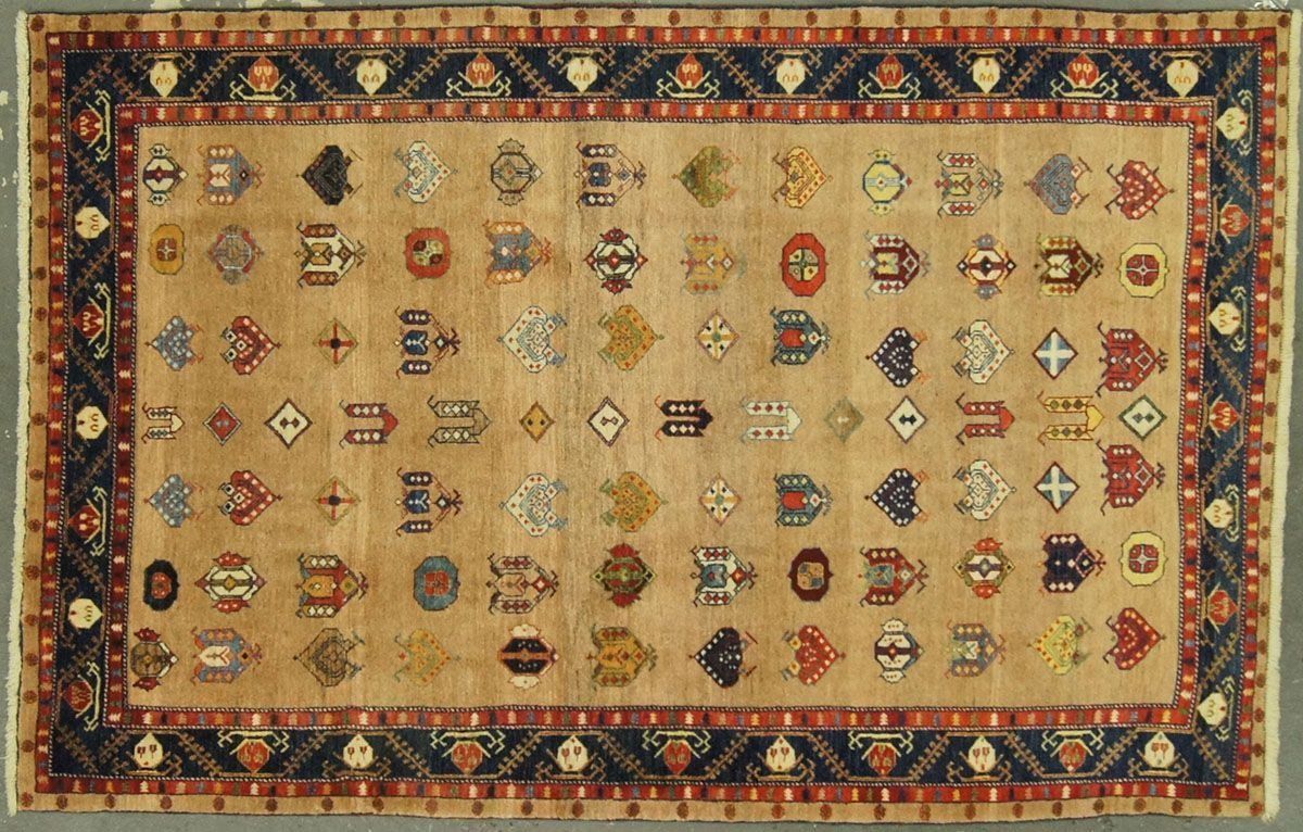 Tan rug with repeating central motifs and dark blue border with red accents.