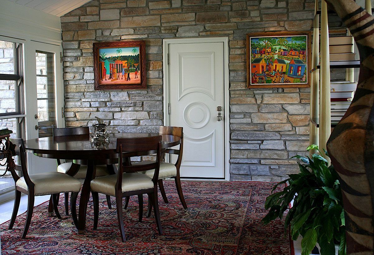 Dining room with stone wall, round table, chairs, and art.